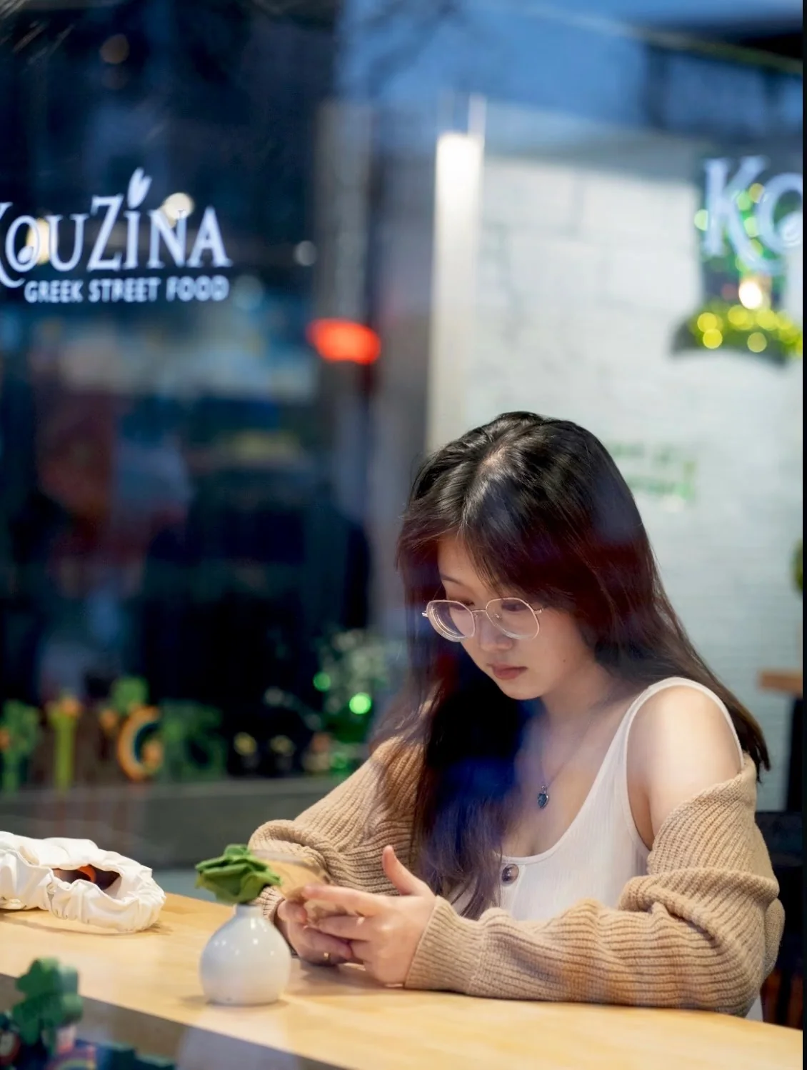A woman looking at her phone beside a café window