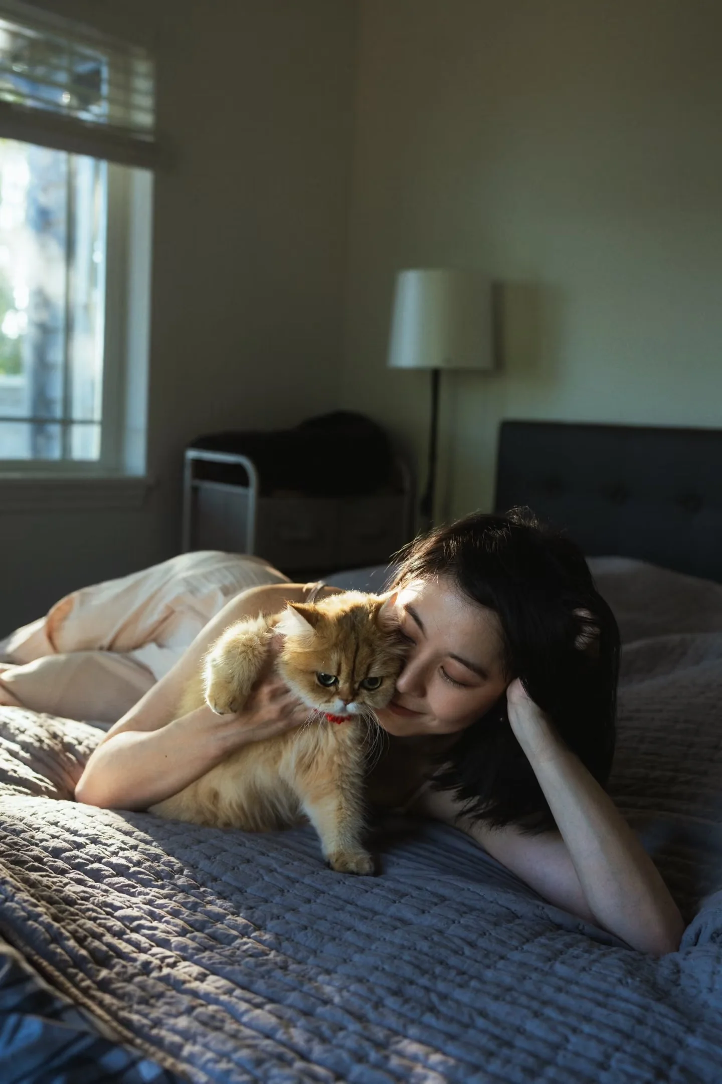 A woman lying on a bed and resting her face beside her cat