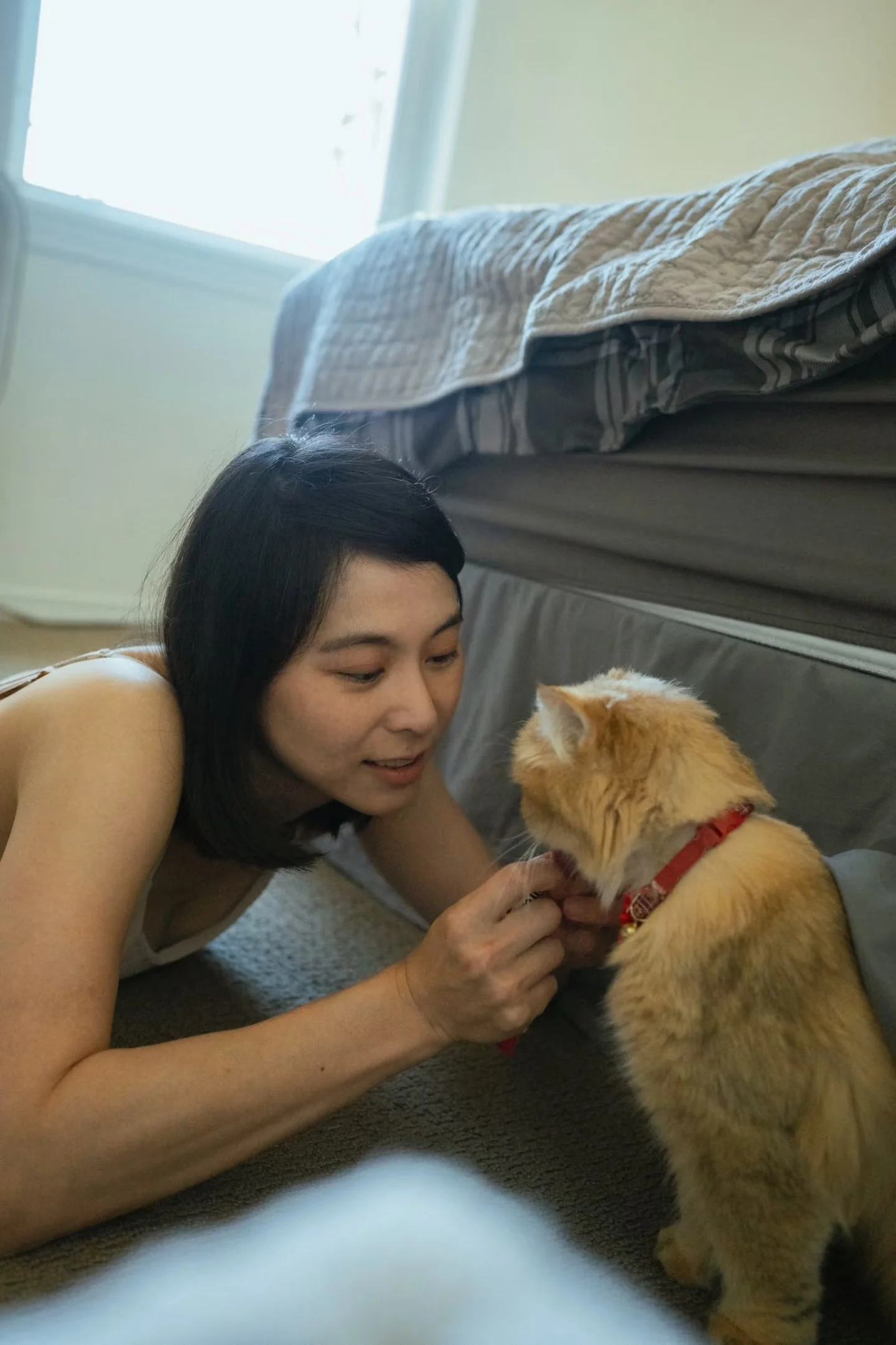 A woman leaning close to a cat beside the bed