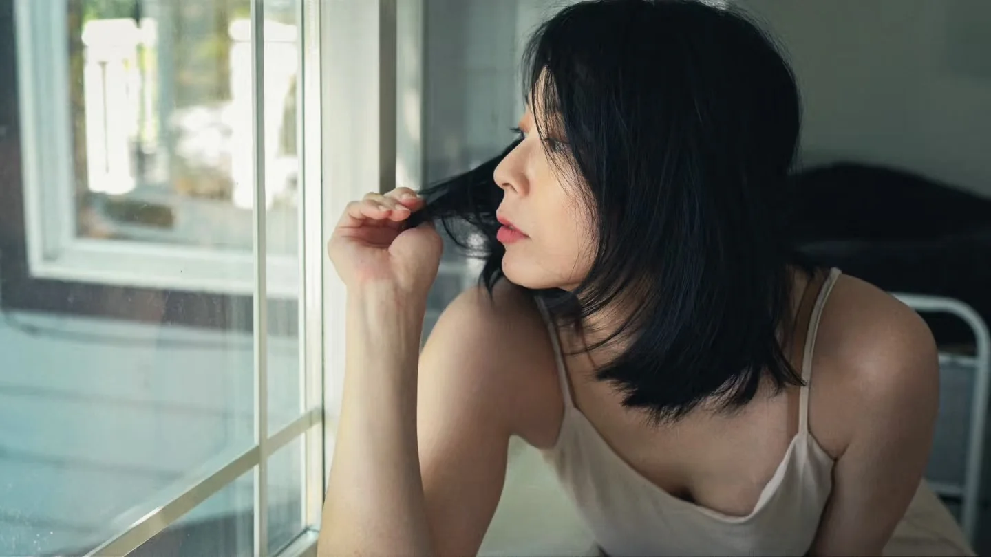 A woman looking through an open window from inside the house
