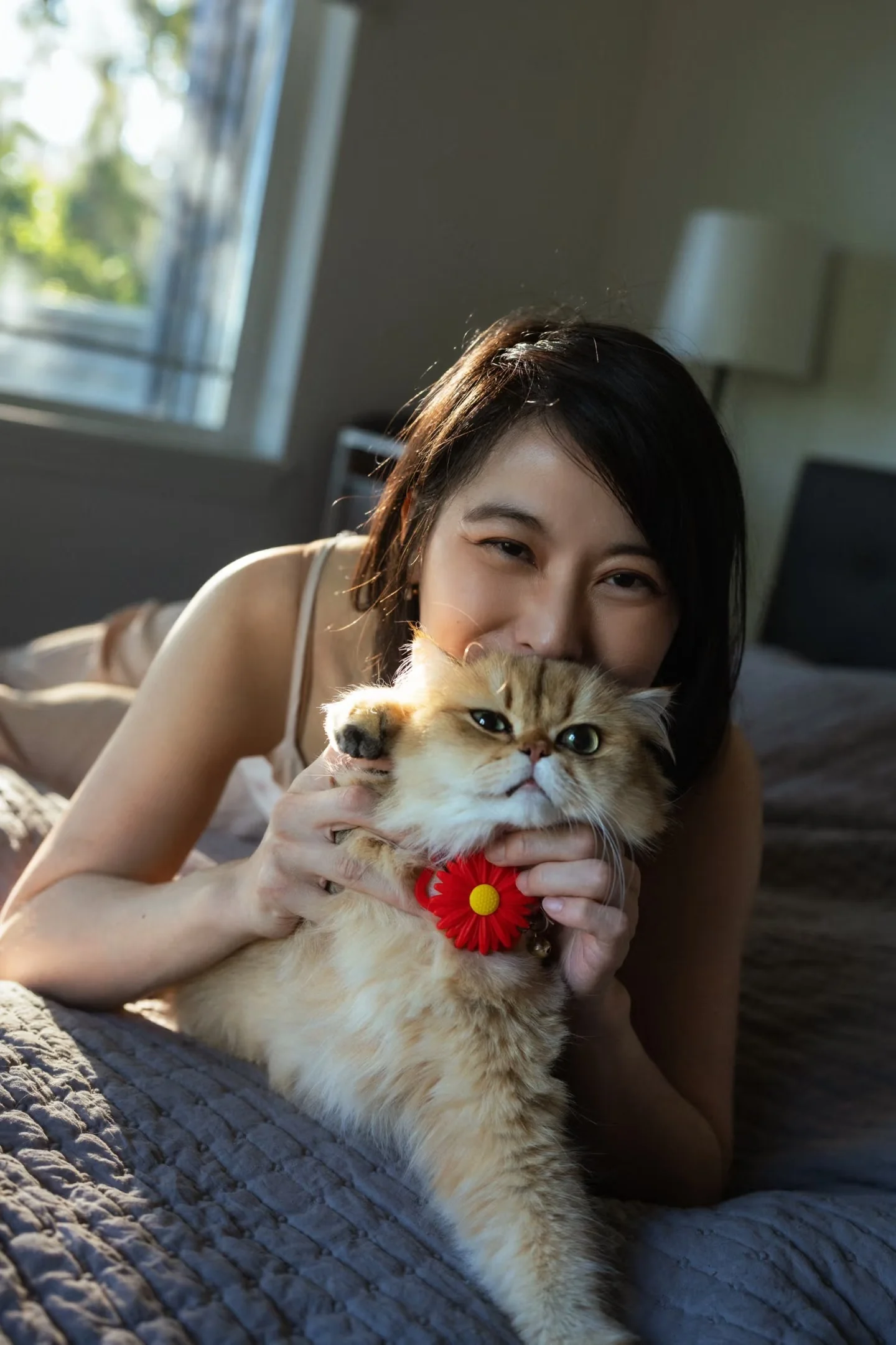 A woman smiling behind an orange cat with a red flower collar