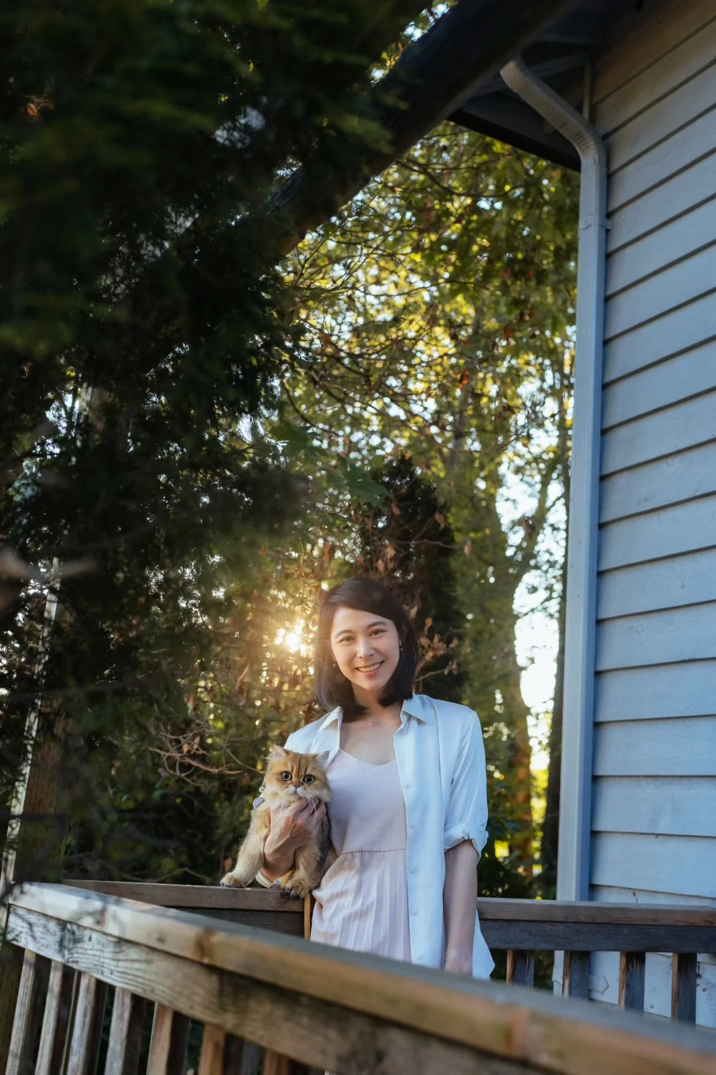 A woman holding a cat on a wooden porch in evening light
