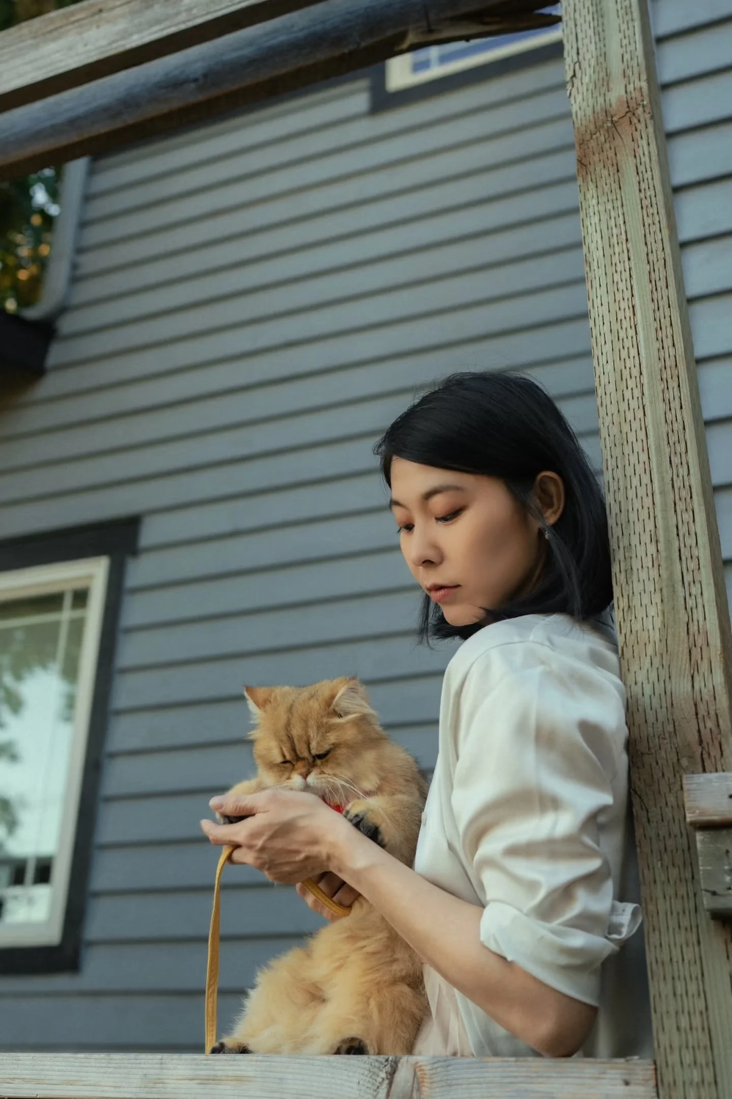 A woman holding her cat against blue house siding