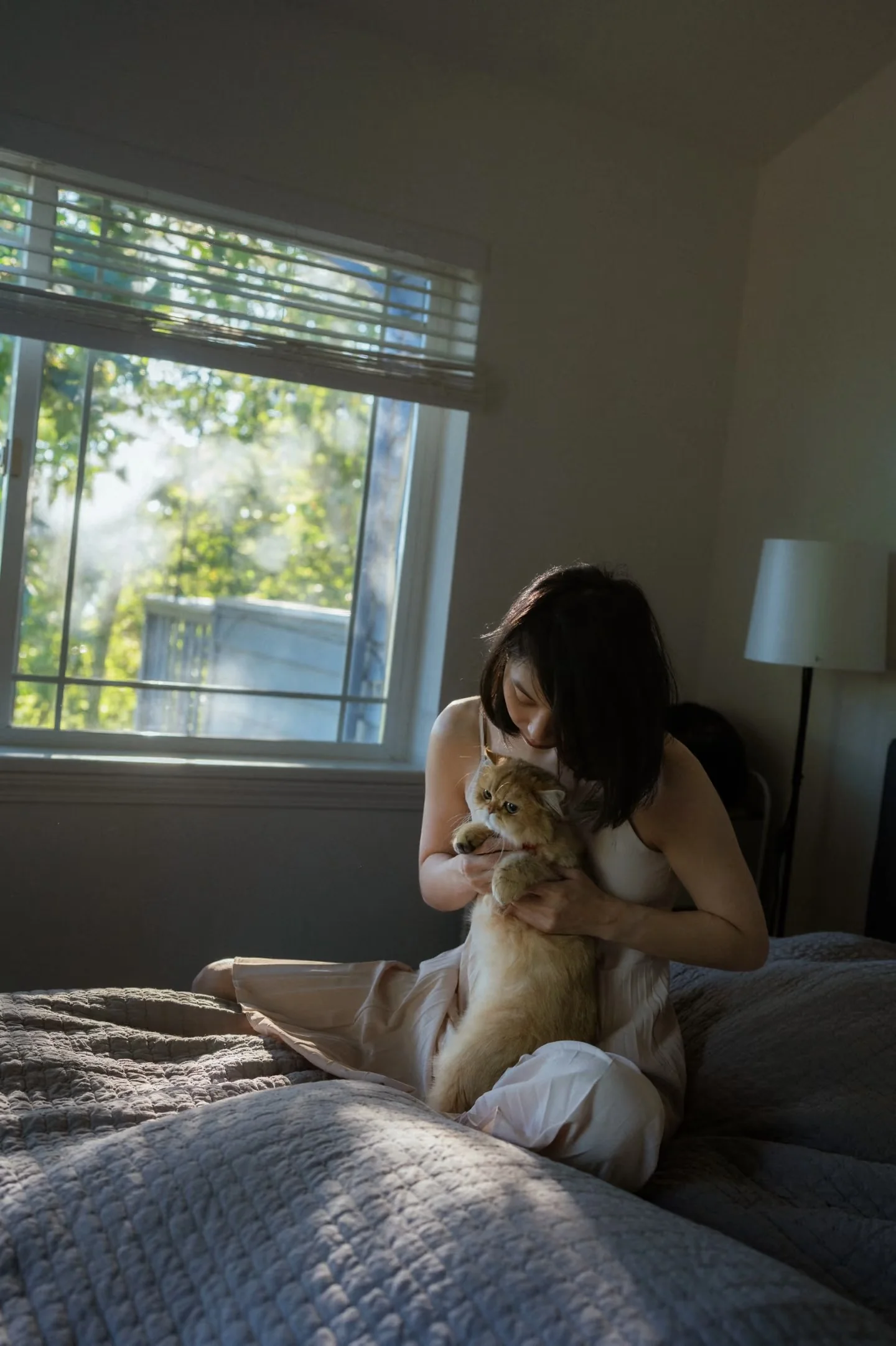 A wide bedroom portrait of a woman holding her cat in window light