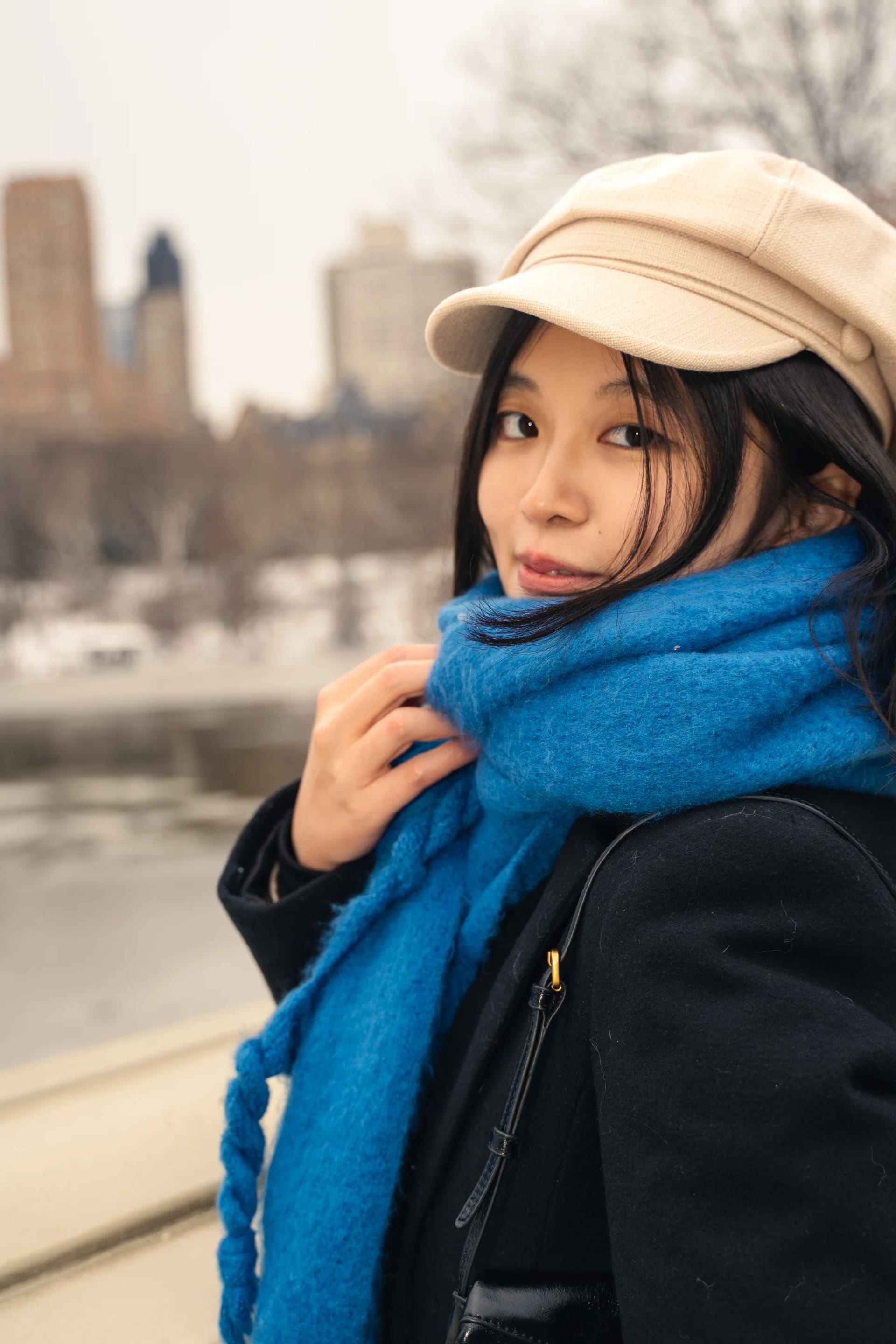 A woman in a cream cap holding a blue scarf beside a stone bridge