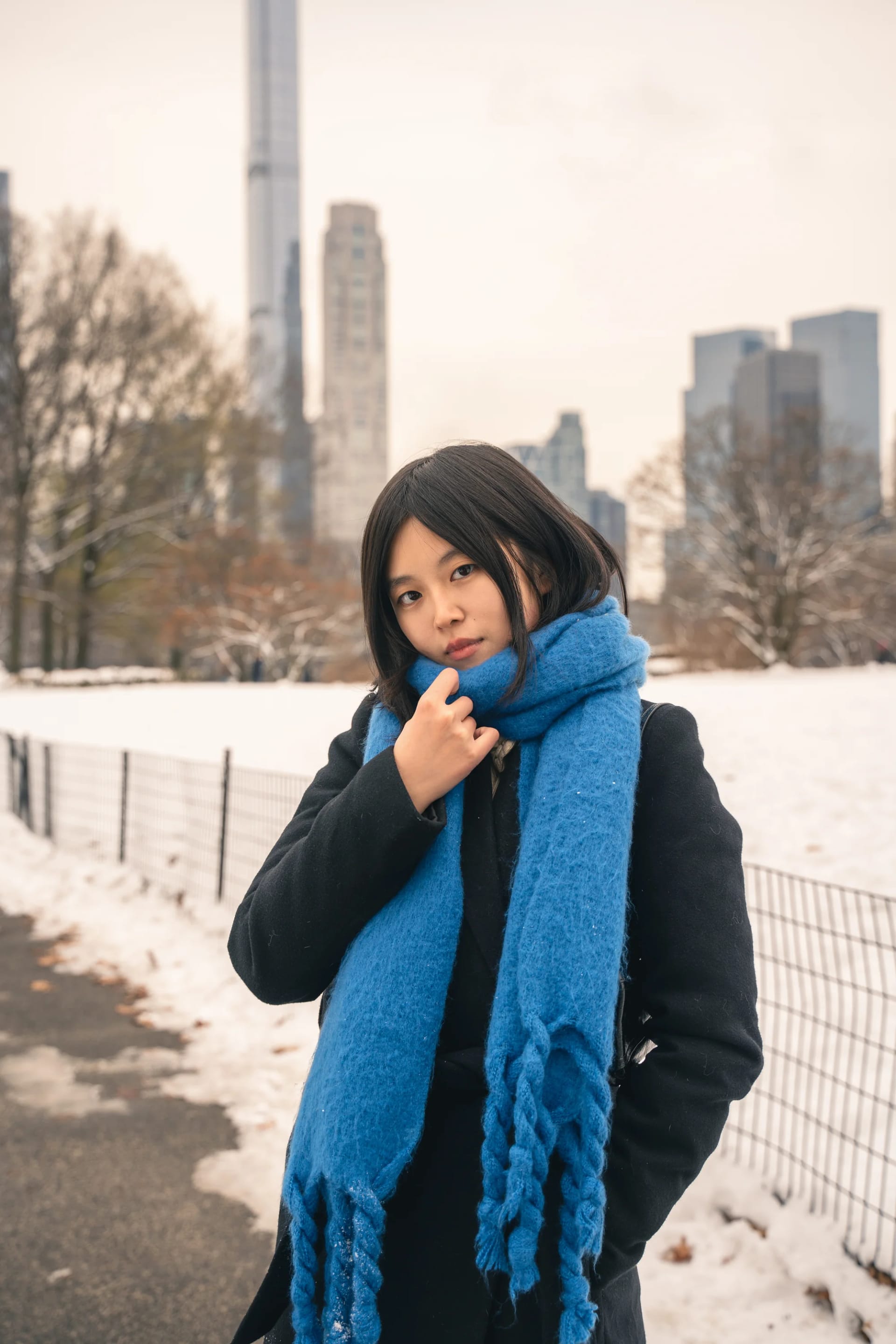 A woman holding her blue scarf on a winter park path