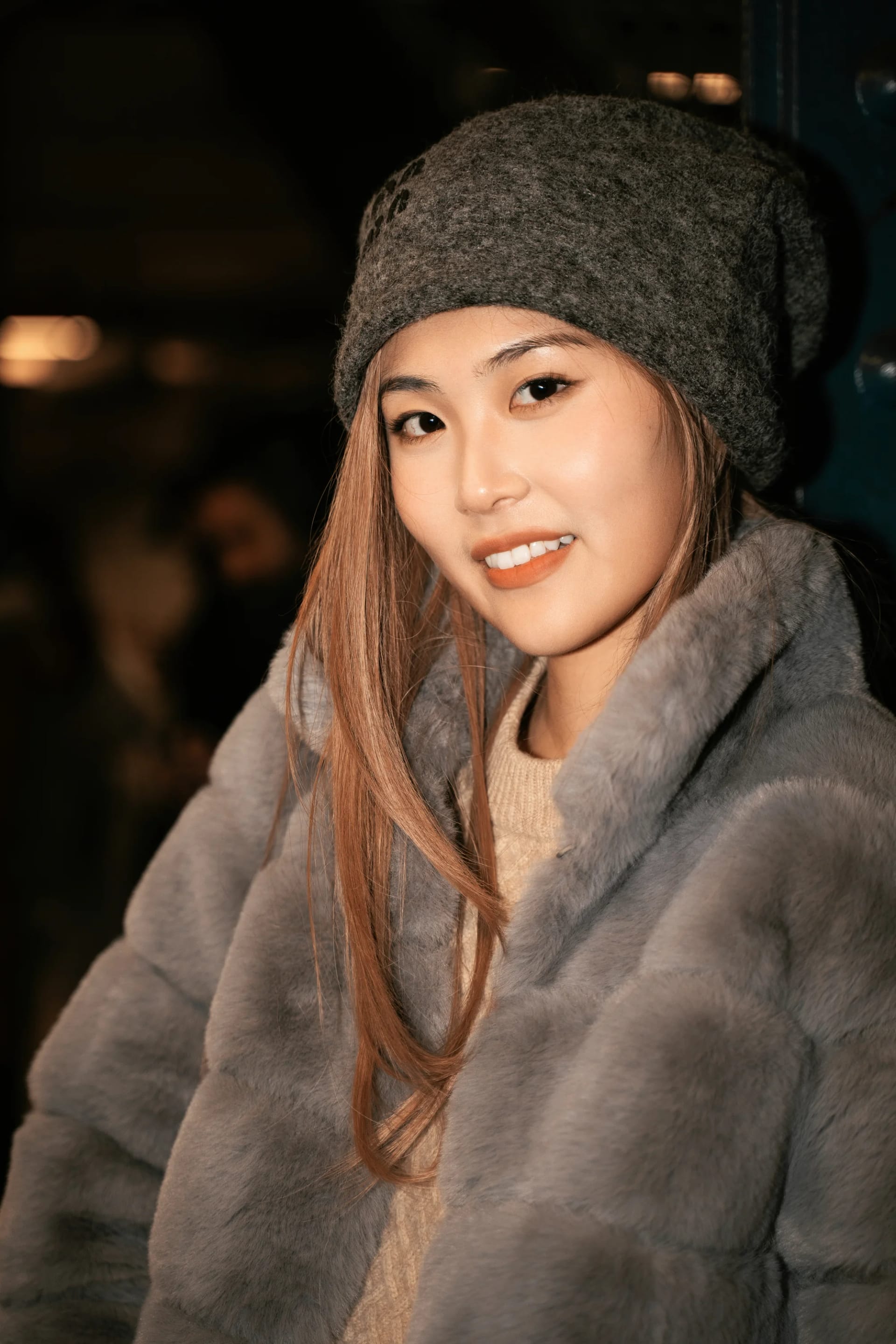A smiling woman in a gray knit hat and soft winter coat