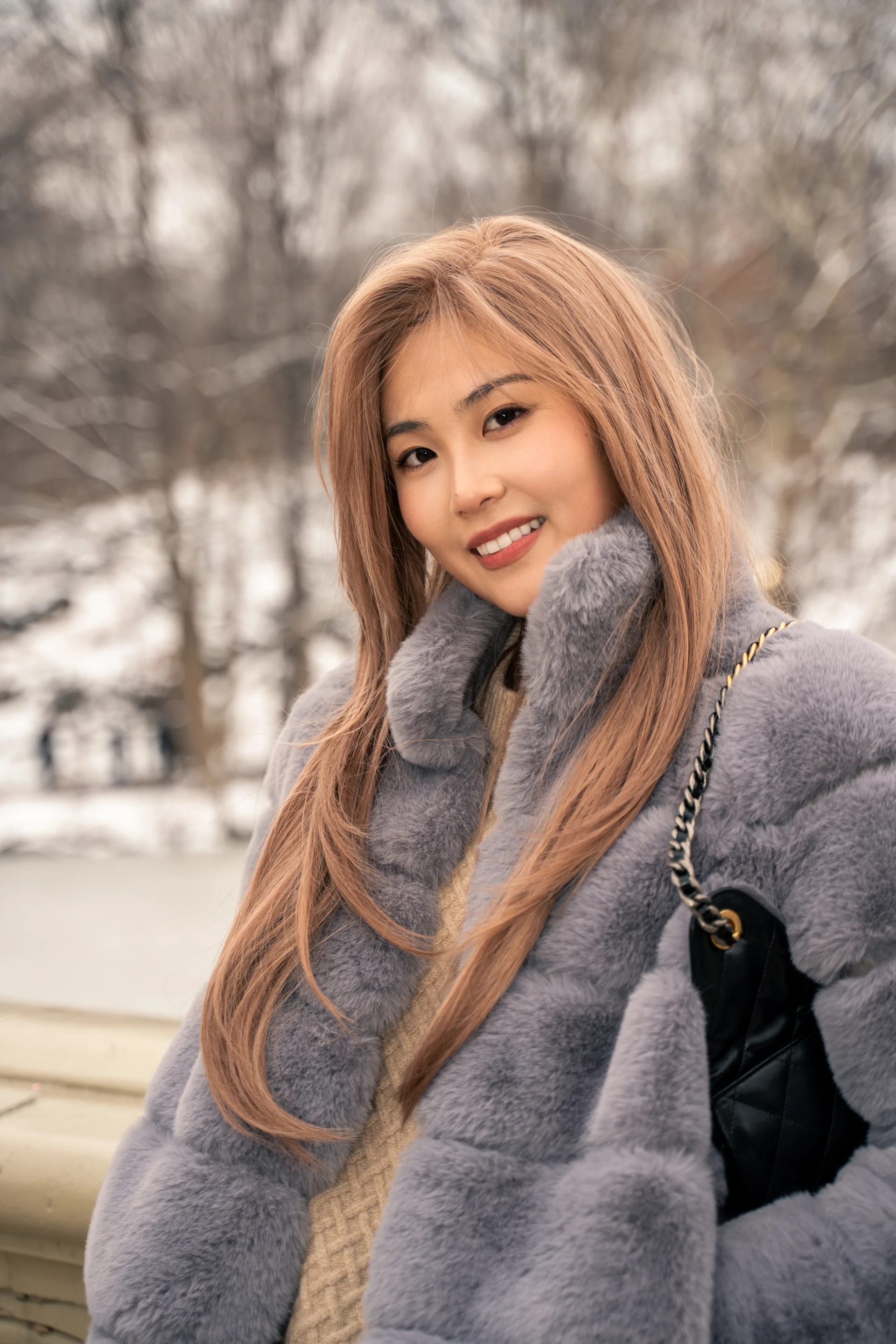 A smiling woman resting her chin on her sleeve beside a stone railing