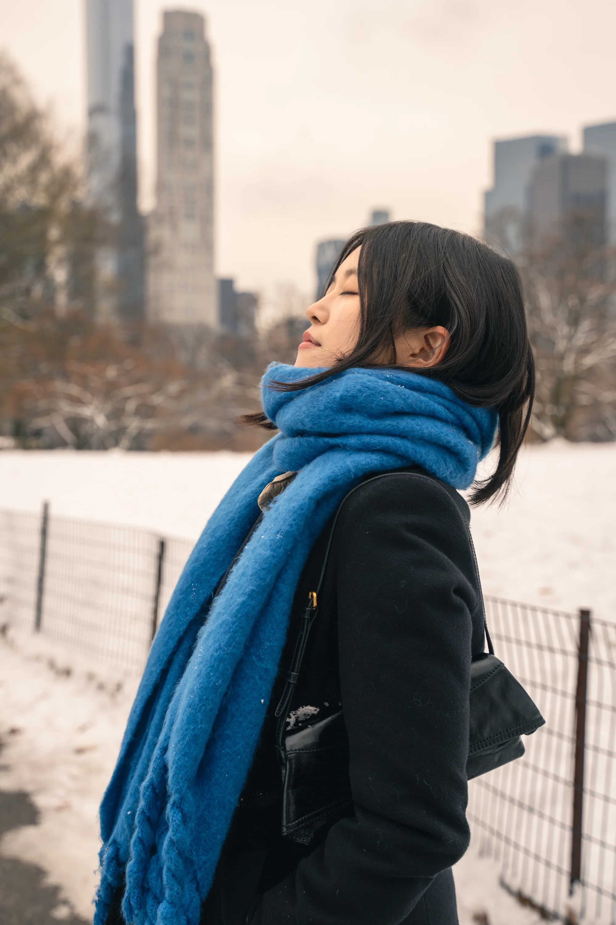 A side portrait of a woman in a blue scarf beside a park fence