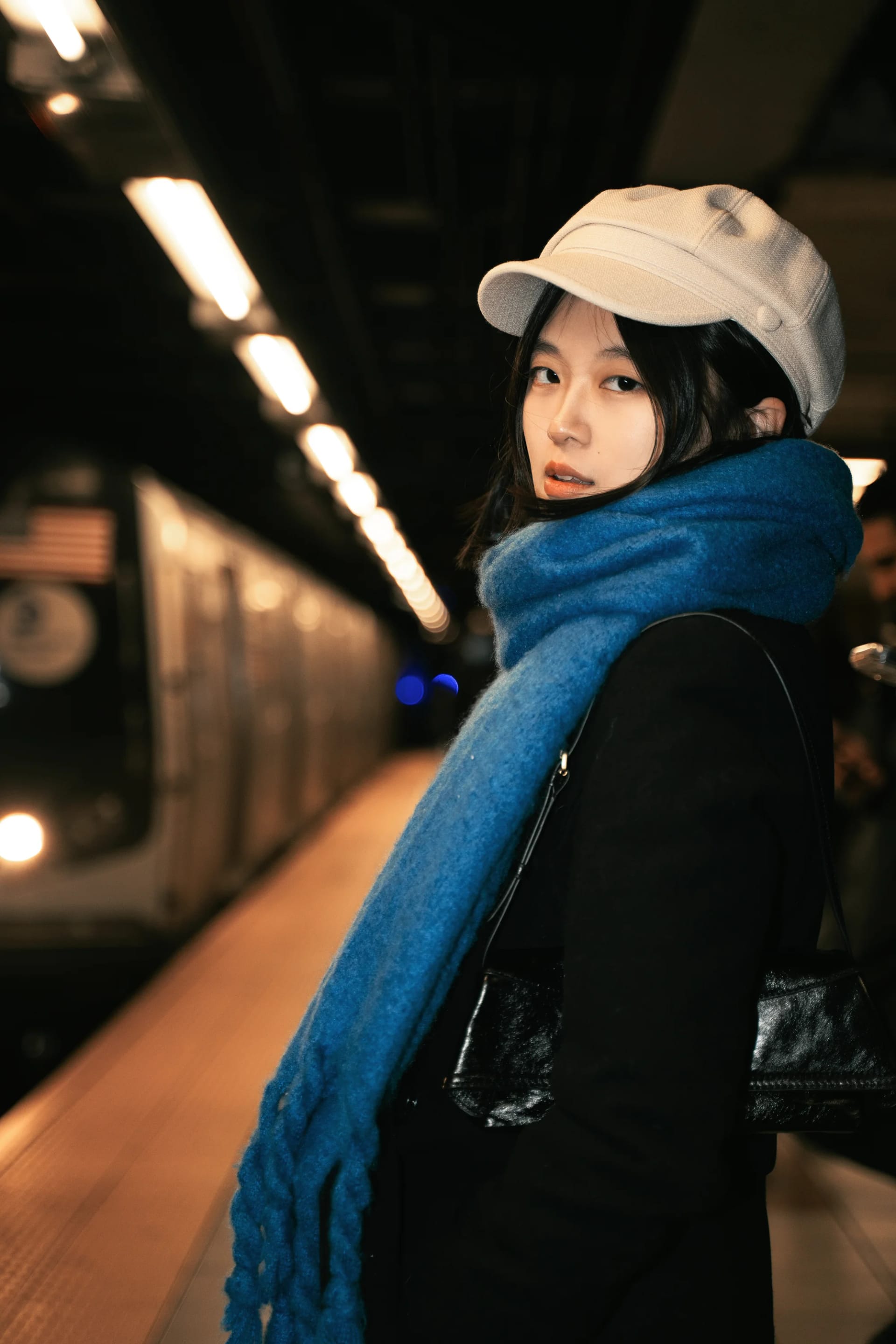 A woman in a cream cap and blue scarf on a subway platform