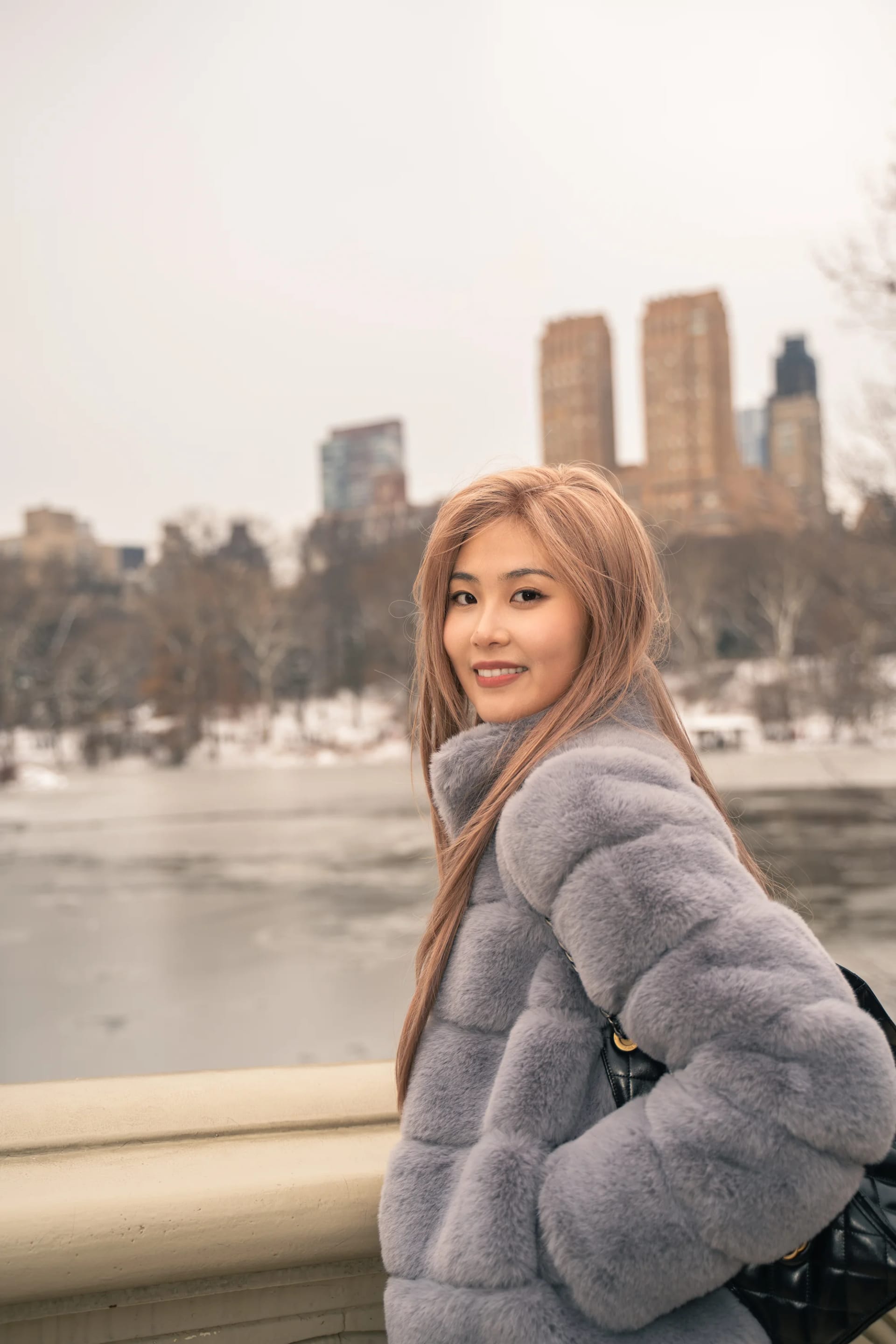 A woman looking back from a stone bridge with city buildings beyond