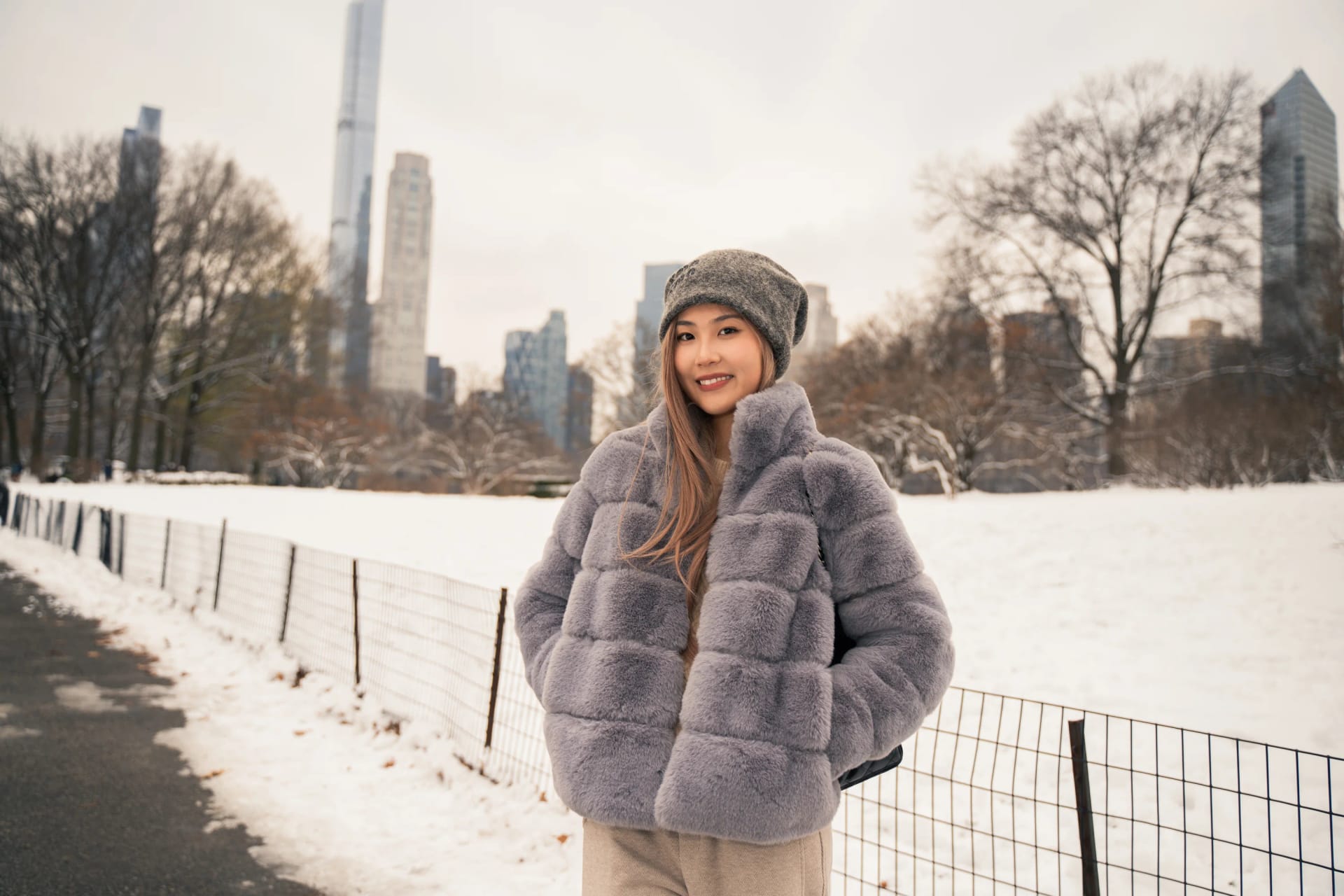 A woman beside a snowy Central Park path with the skyline behind her