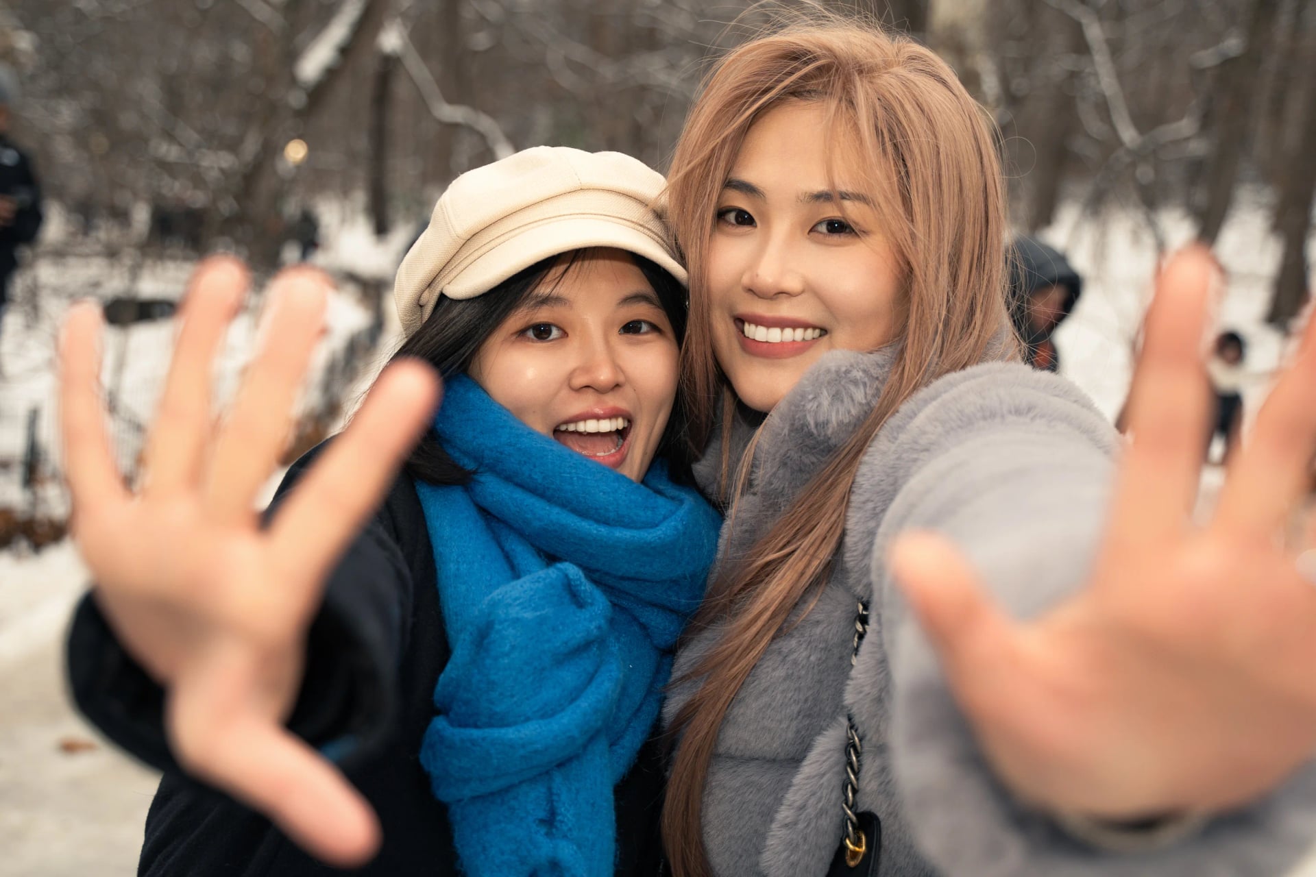 Two friends reaching toward the camera in a snowy park
