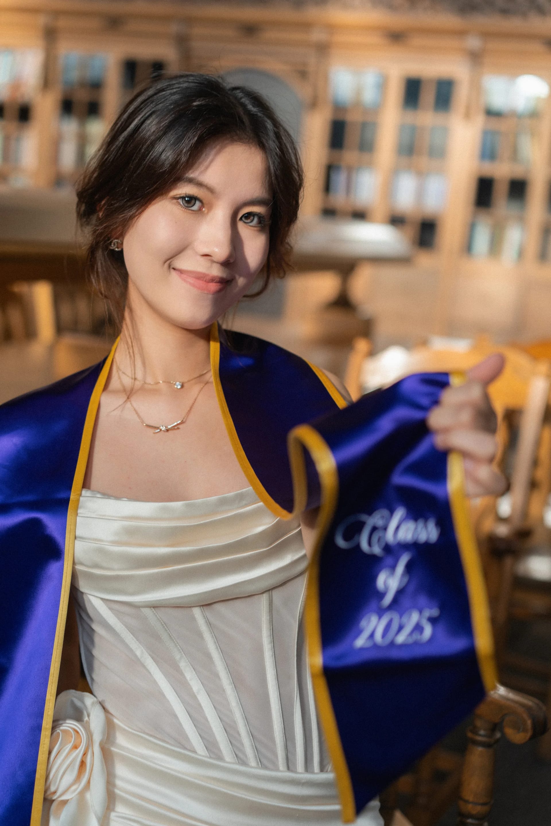 A graduate showing her Class of 2025 sash in a reading room
