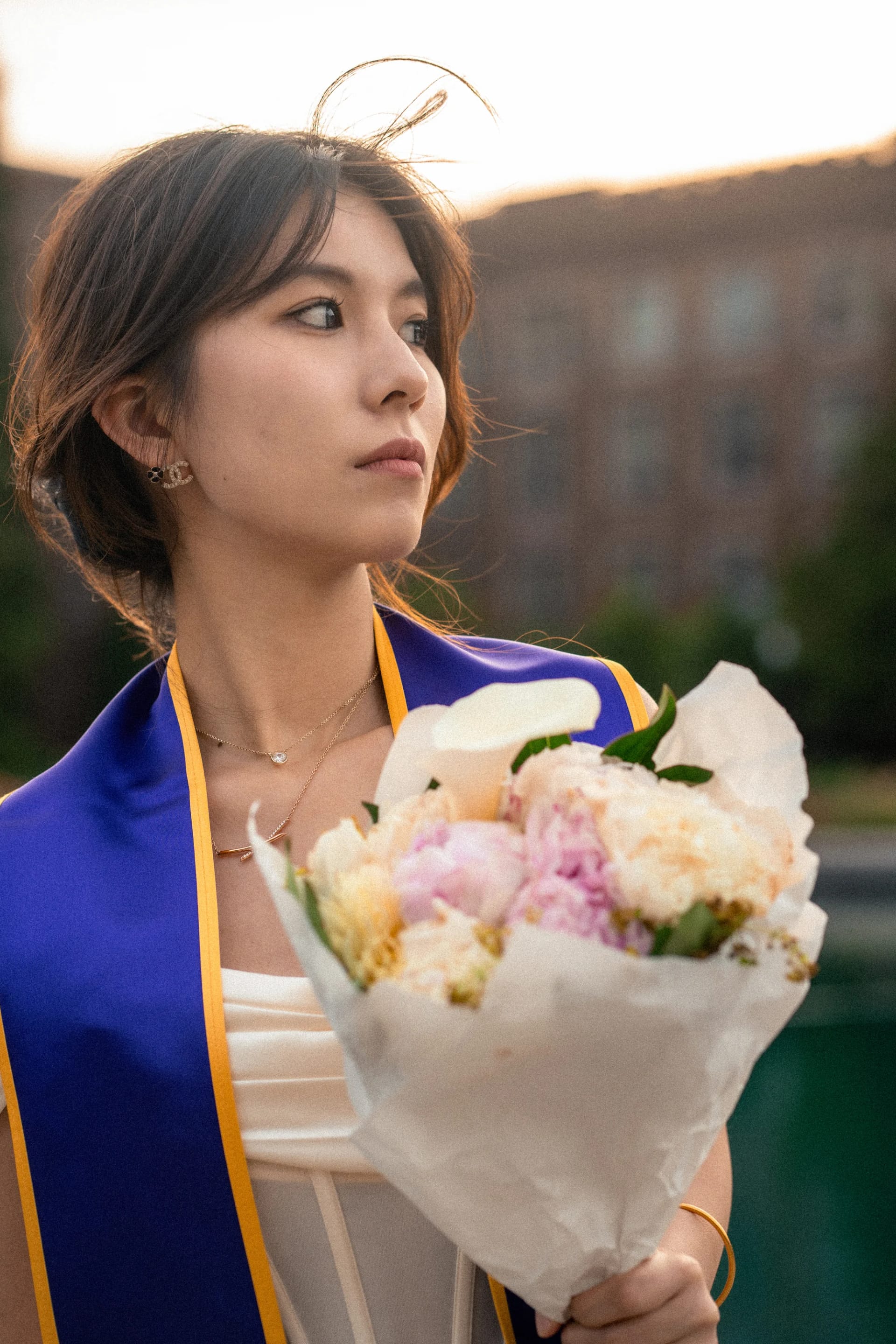 A close portrait of a graduate holding a bouquet outdoors