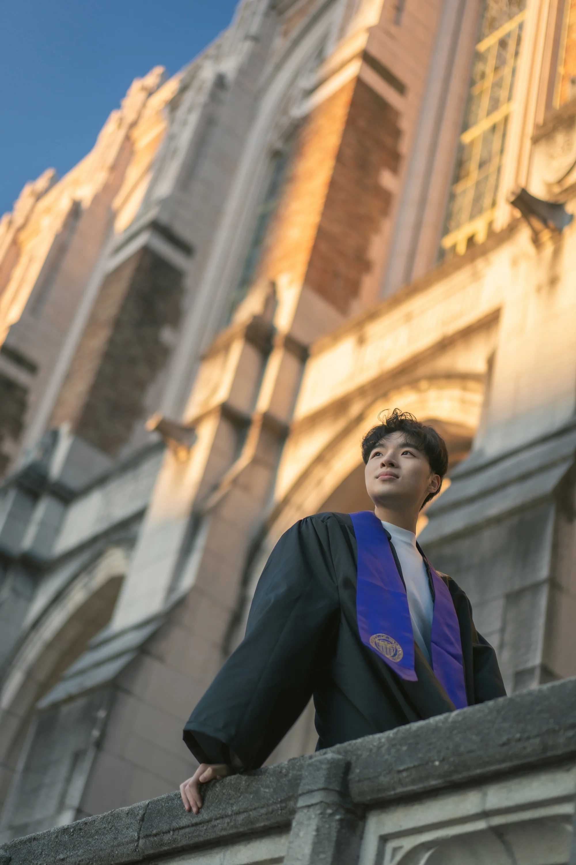A low-angle portrait of a graduate beside a sunlit campus building