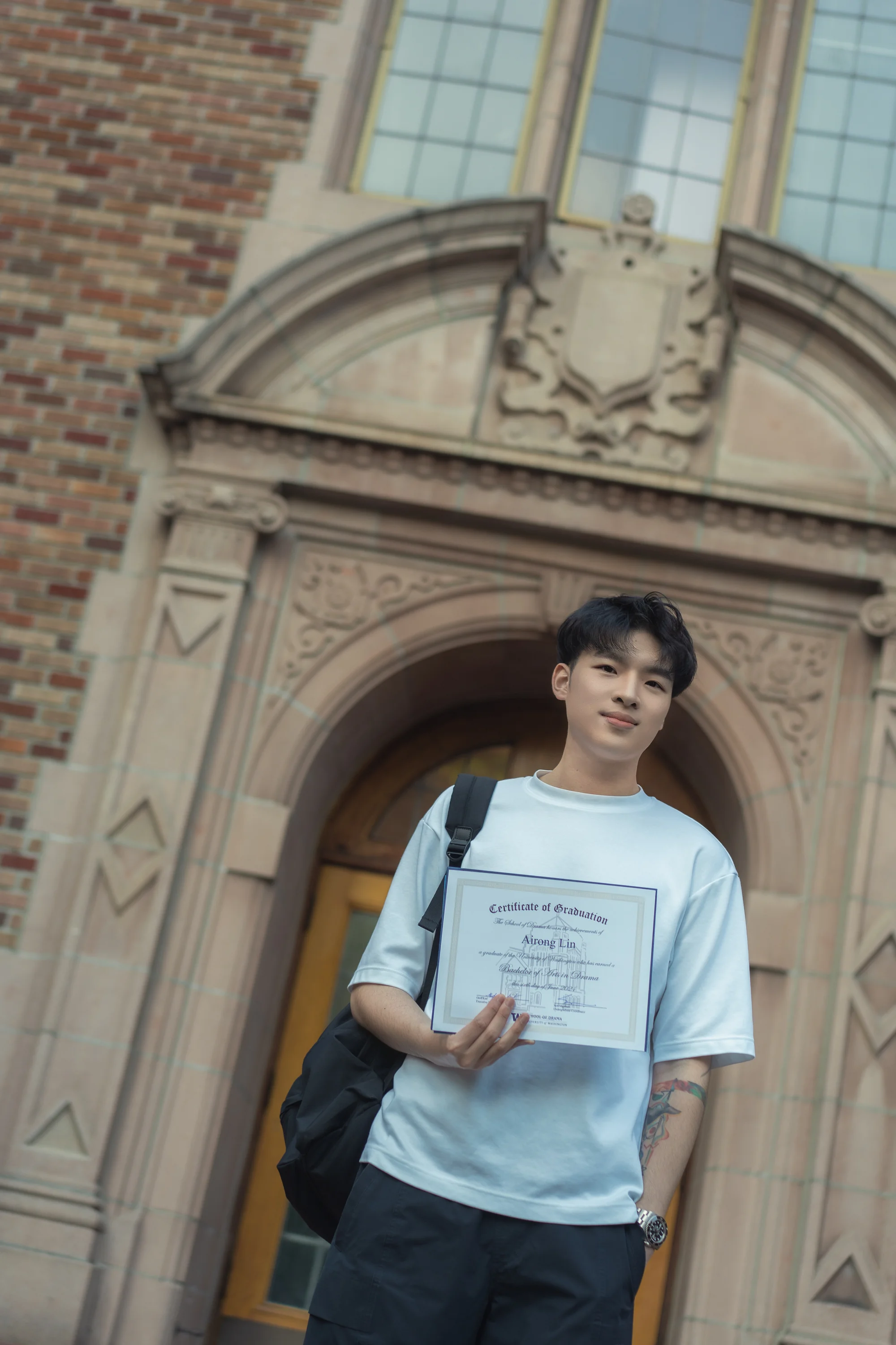A graduate holding a diploma beneath a brick archway