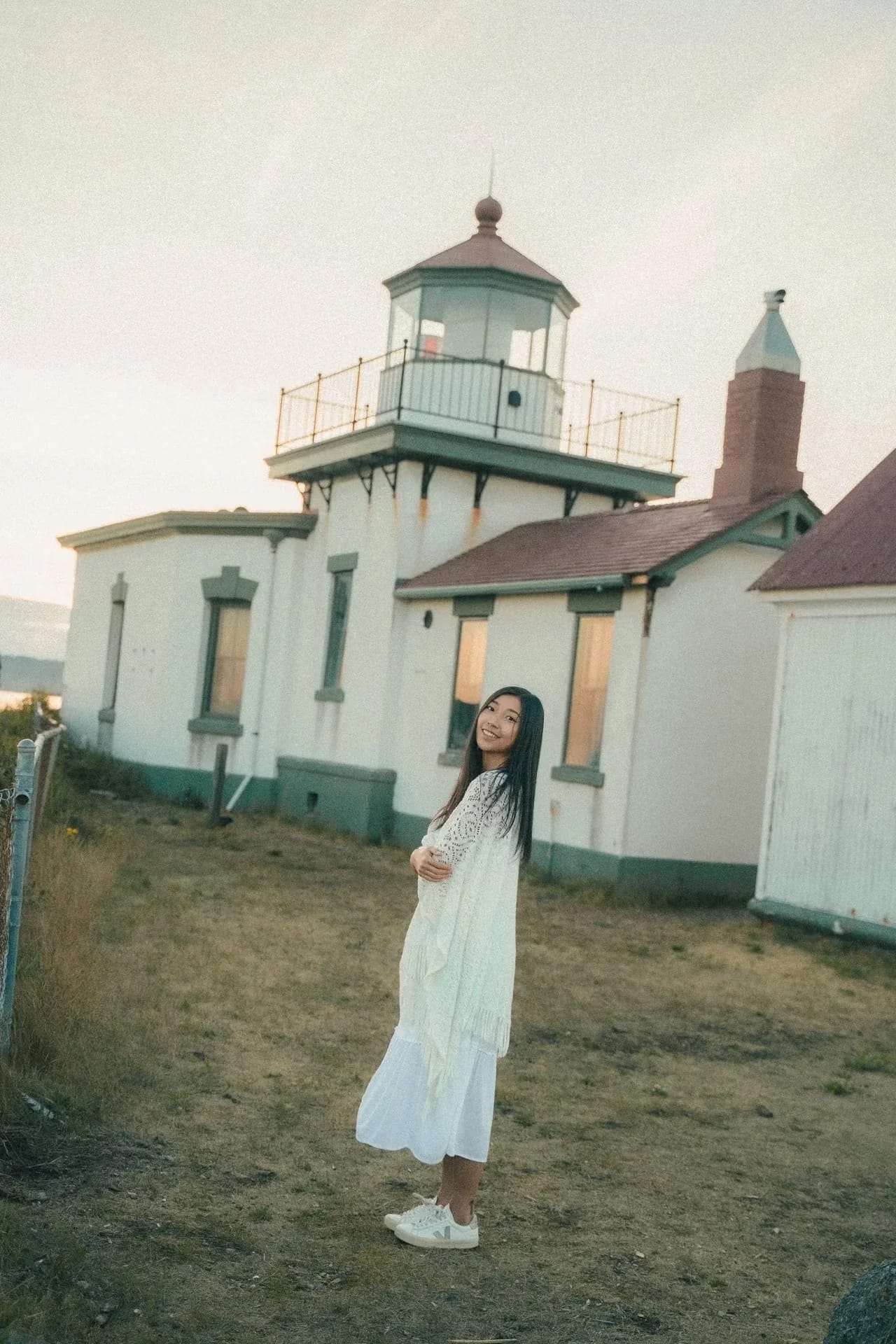 A woman in a white dress standing in front of a lighthouse