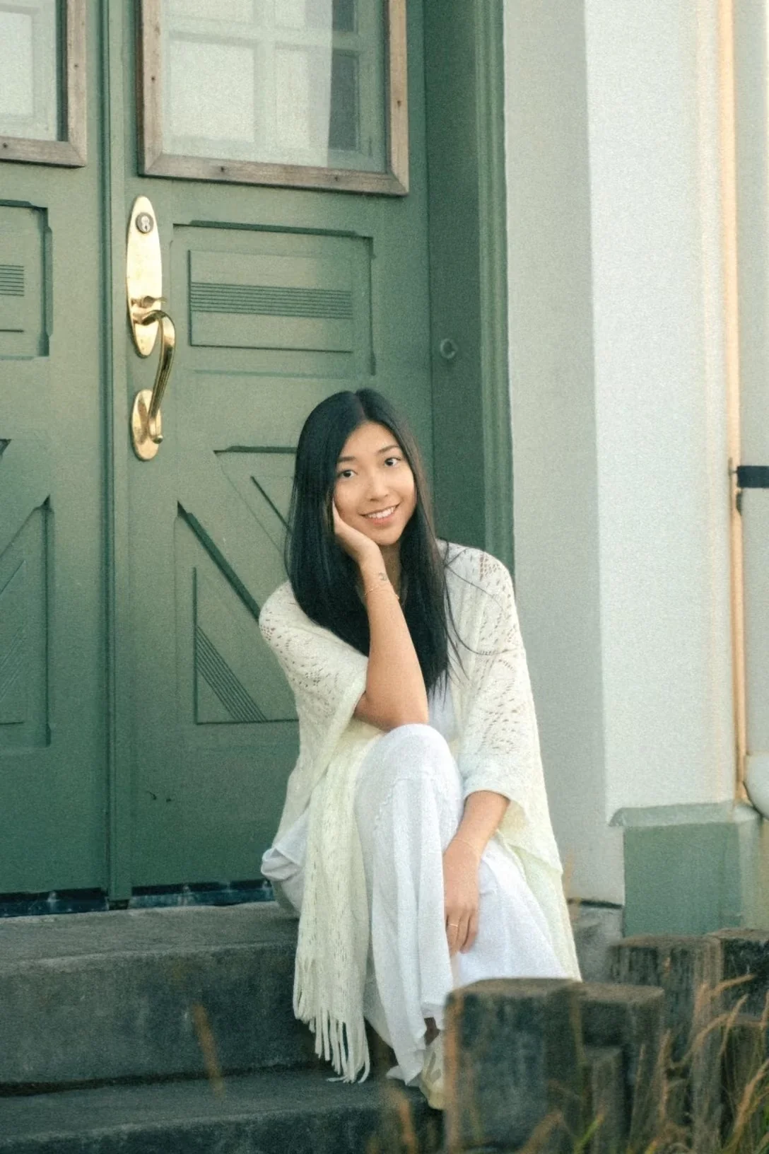 A woman in a white dress seated beside a green door