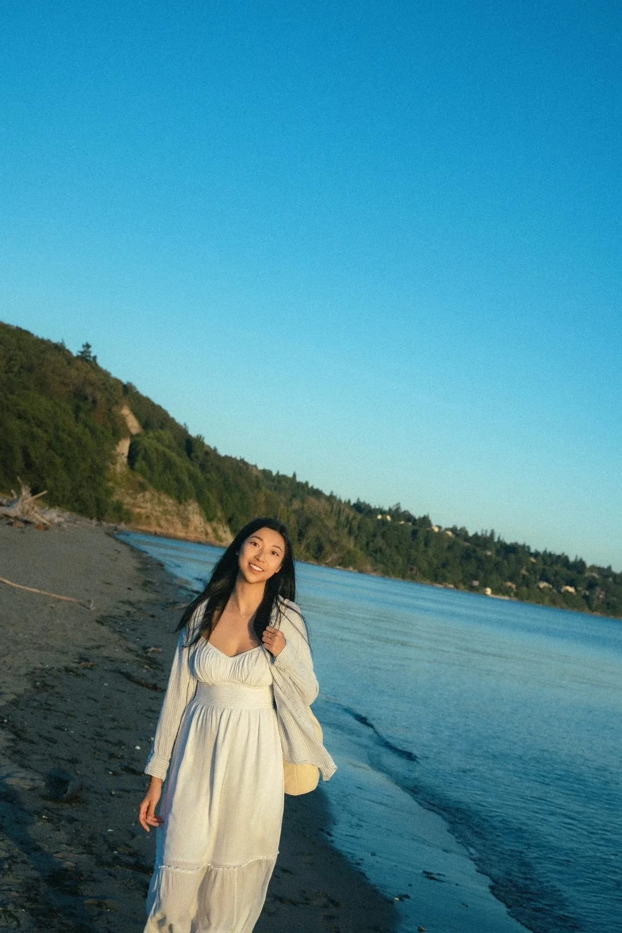 A woman smiling beside a quiet blue shoreline