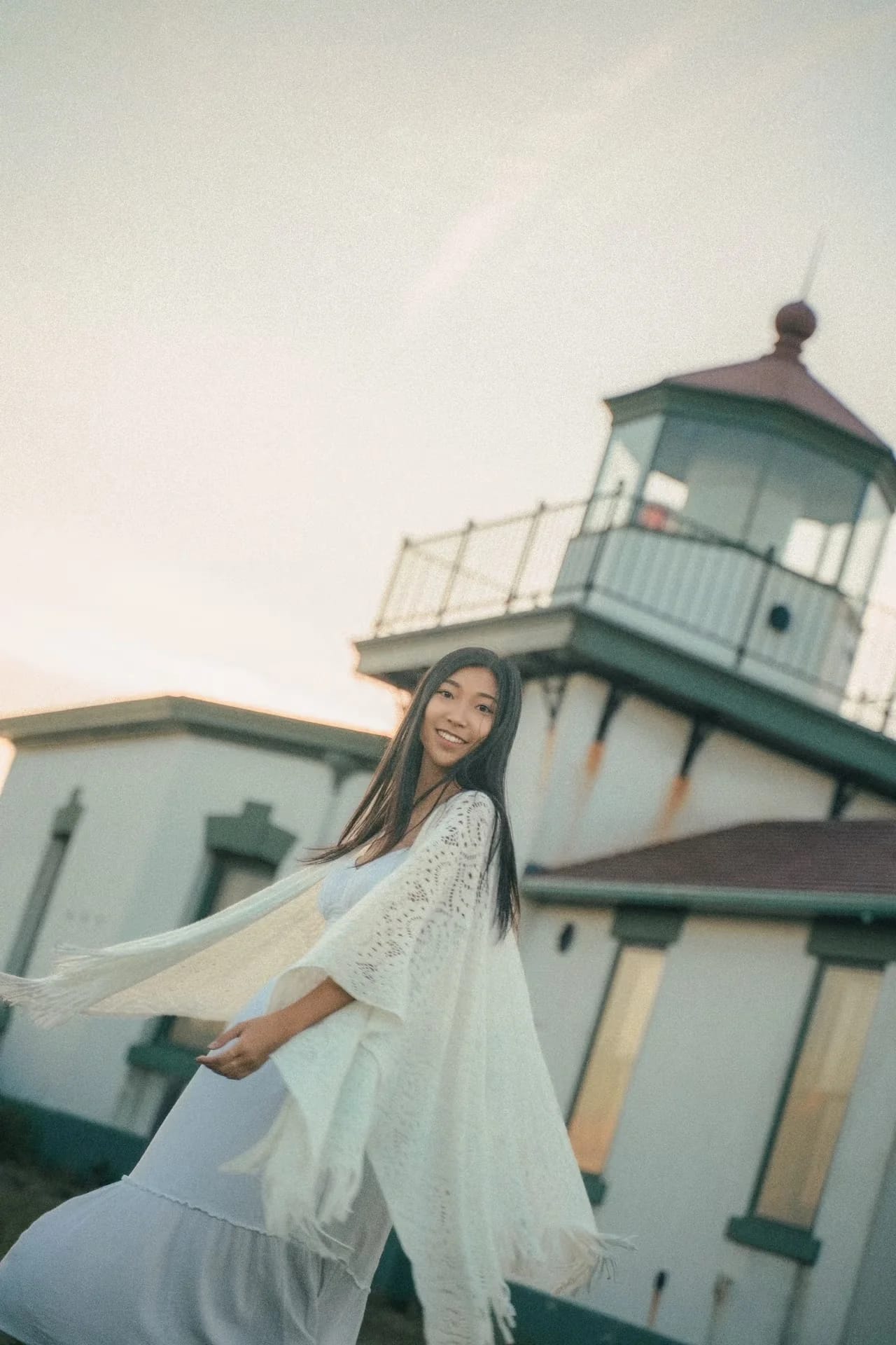 A woman reaching toward the camera with a lighthouse behind her