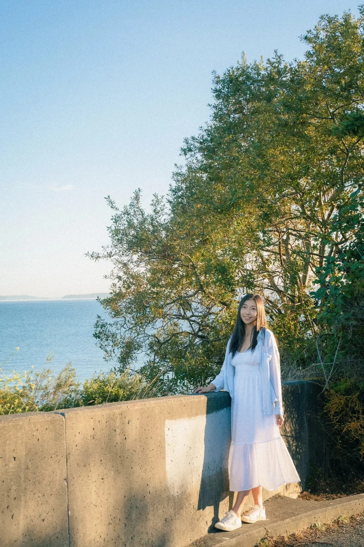 A woman standing beside a stone wall under tall trees