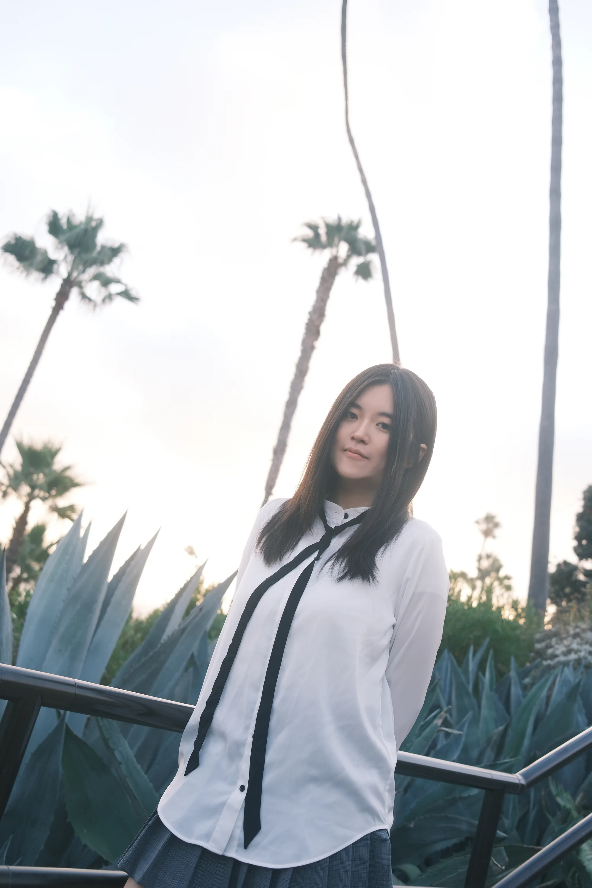 A portrait in a white shirt beside a palm-lined coastal railing