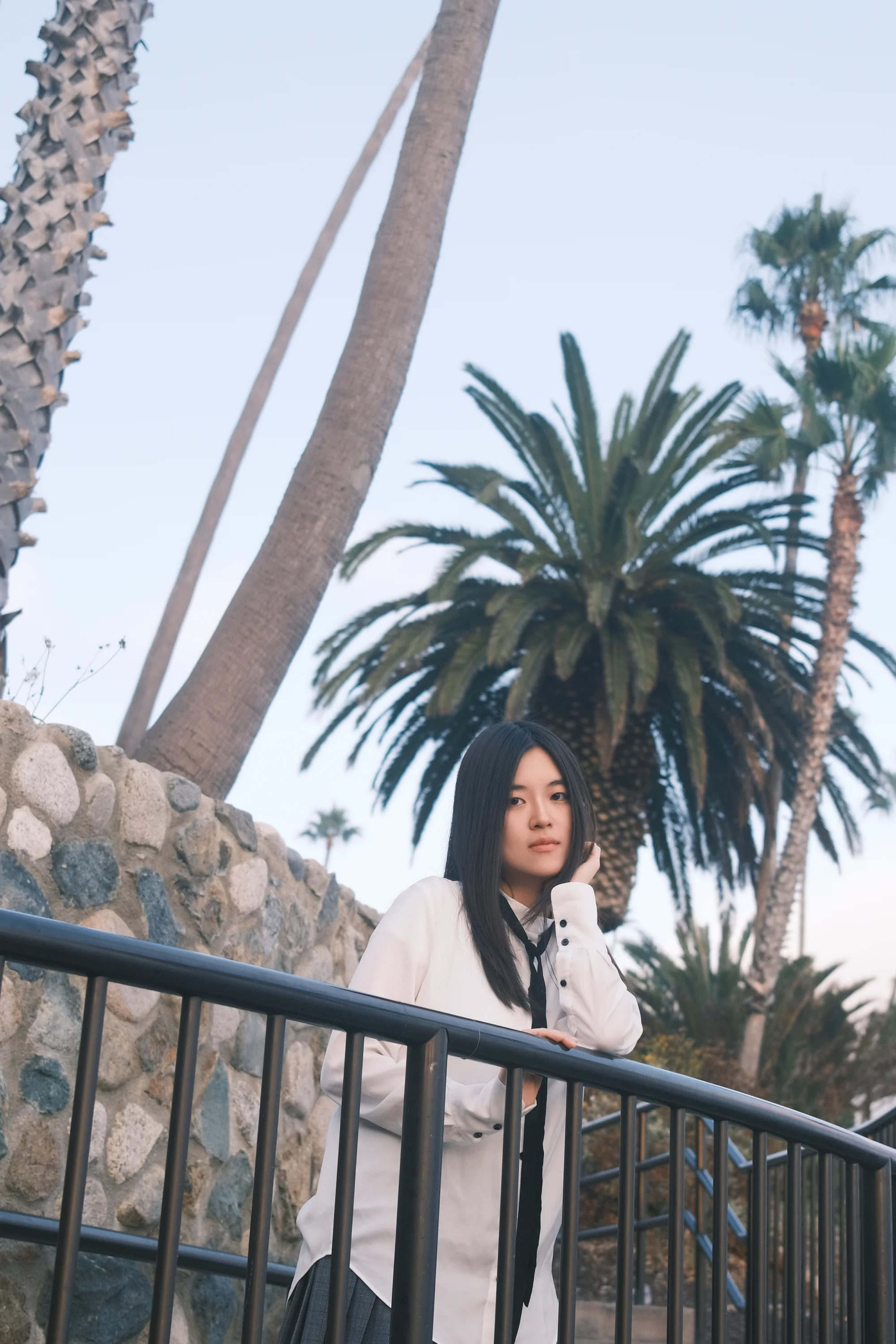 A portrait leaning against a railing beneath tall palms