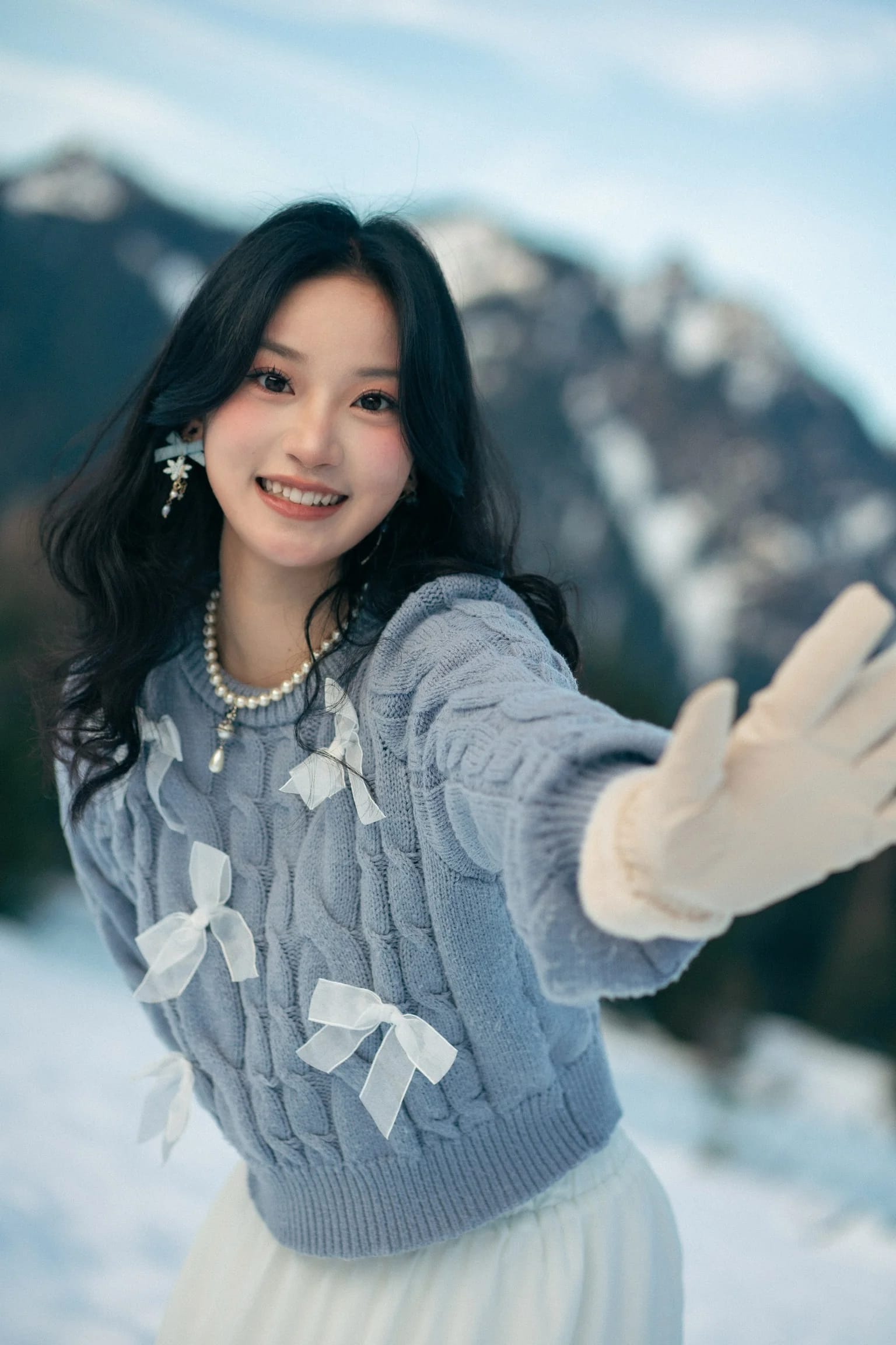 A woman smiling and reaching a mitten toward the camera