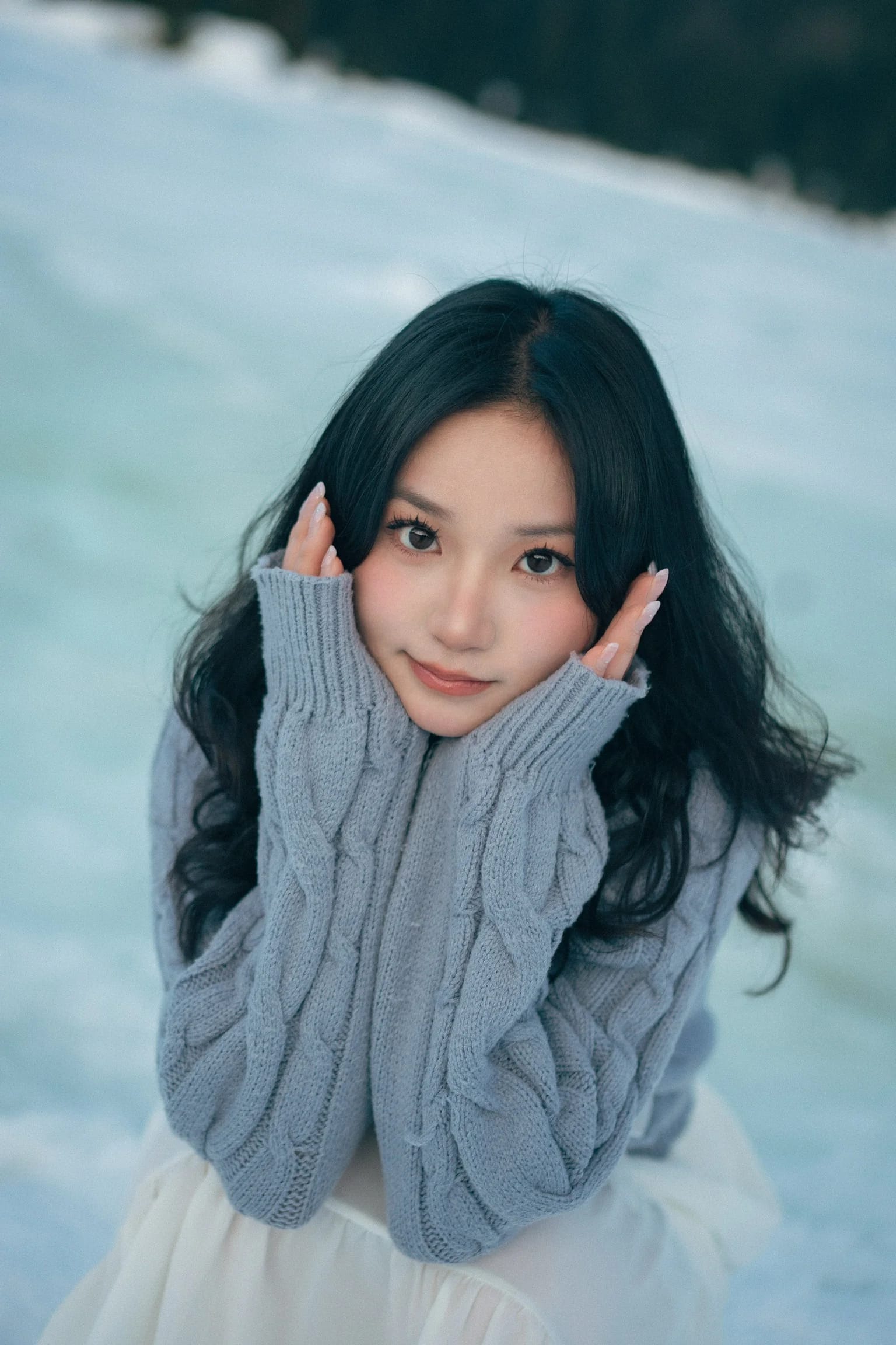 A woman in a blue sweater resting her chin in her hands