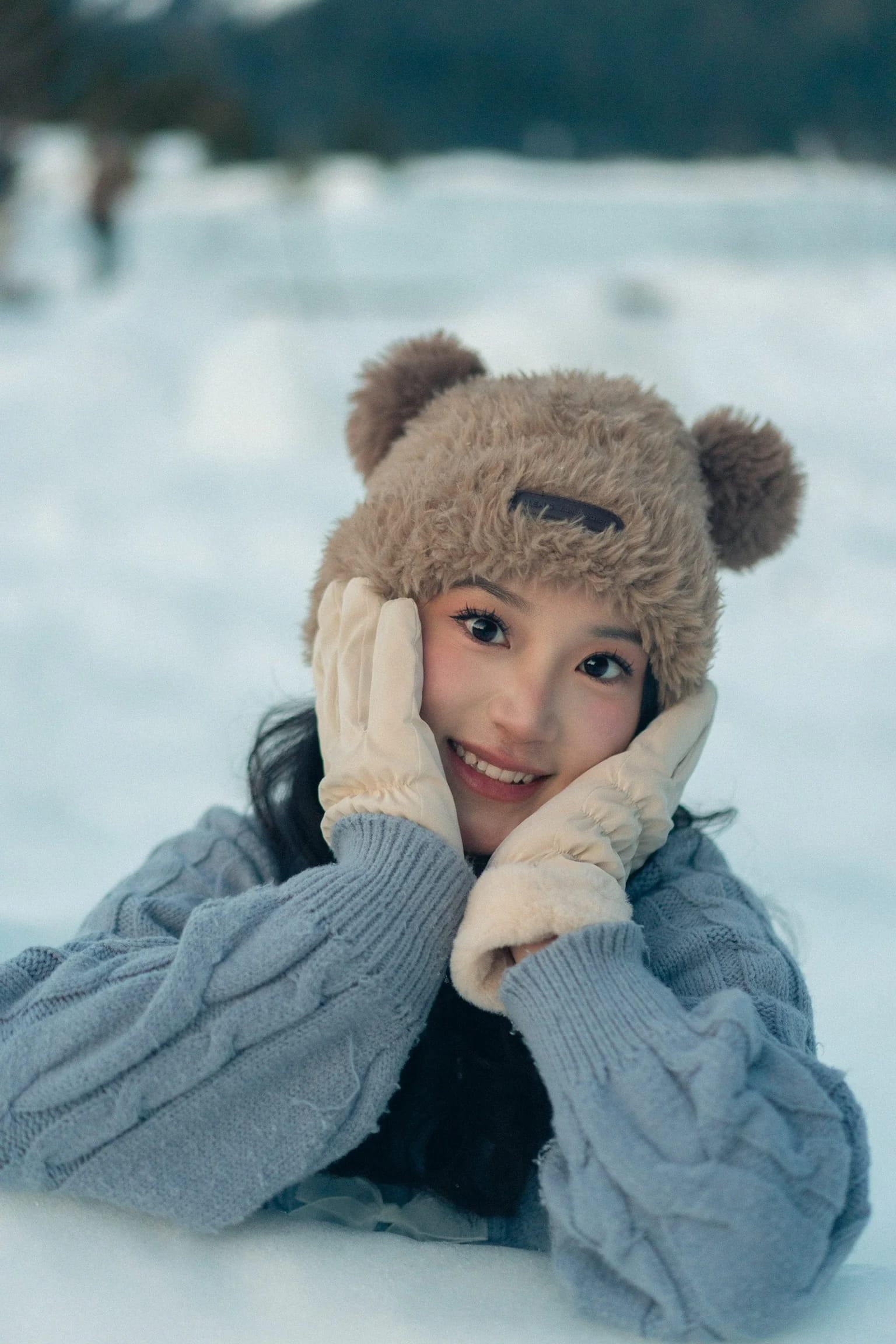 A woman resting her face in mittens while wearing a bear-ear hat