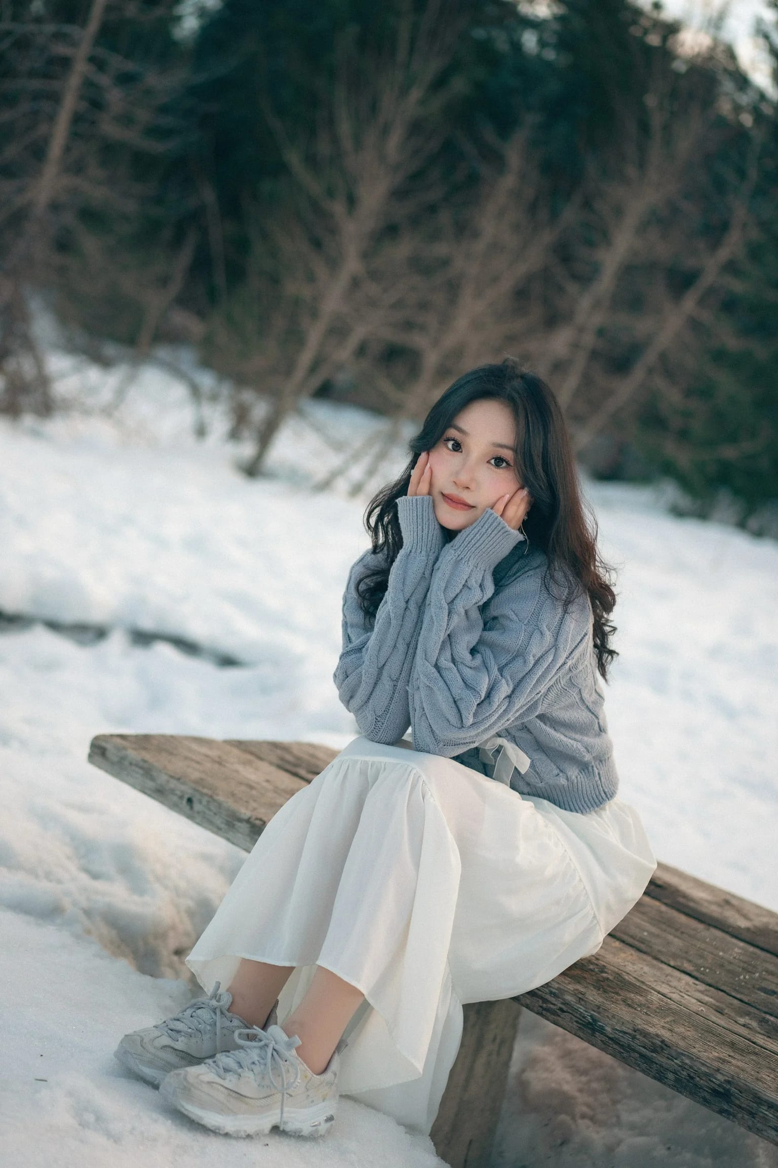 A full-length portrait of a woman on a bench beside the snow