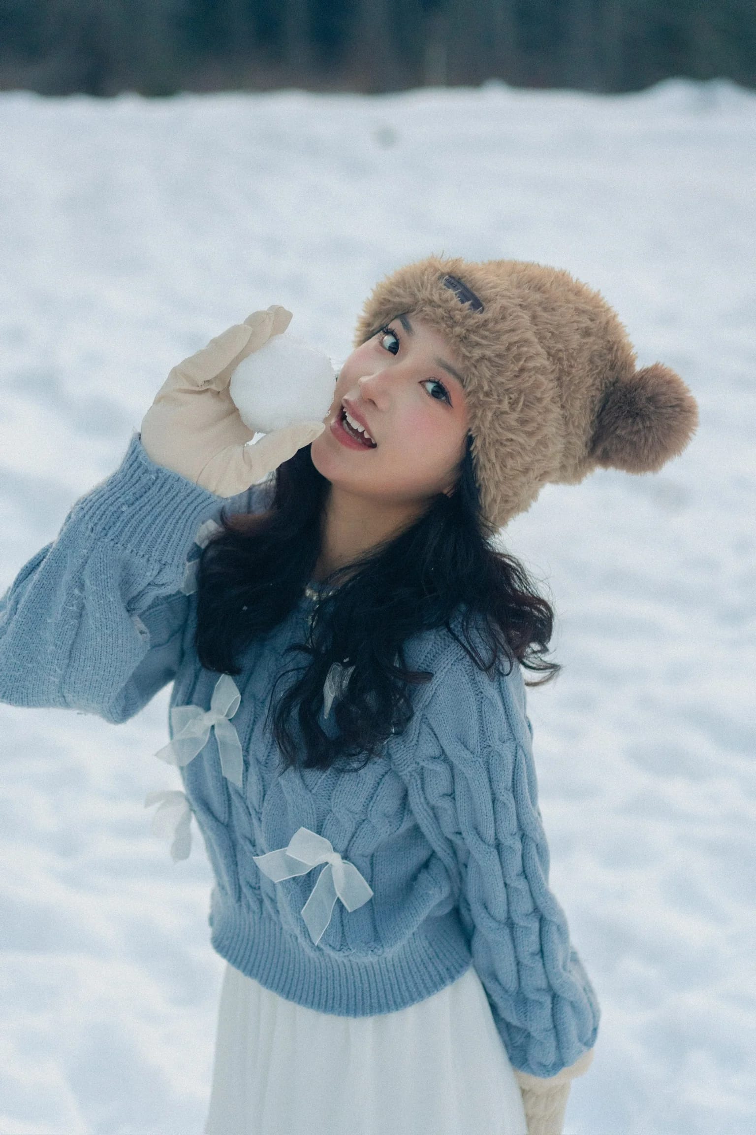 A woman looking upward with her bear-ear hat framed by snow