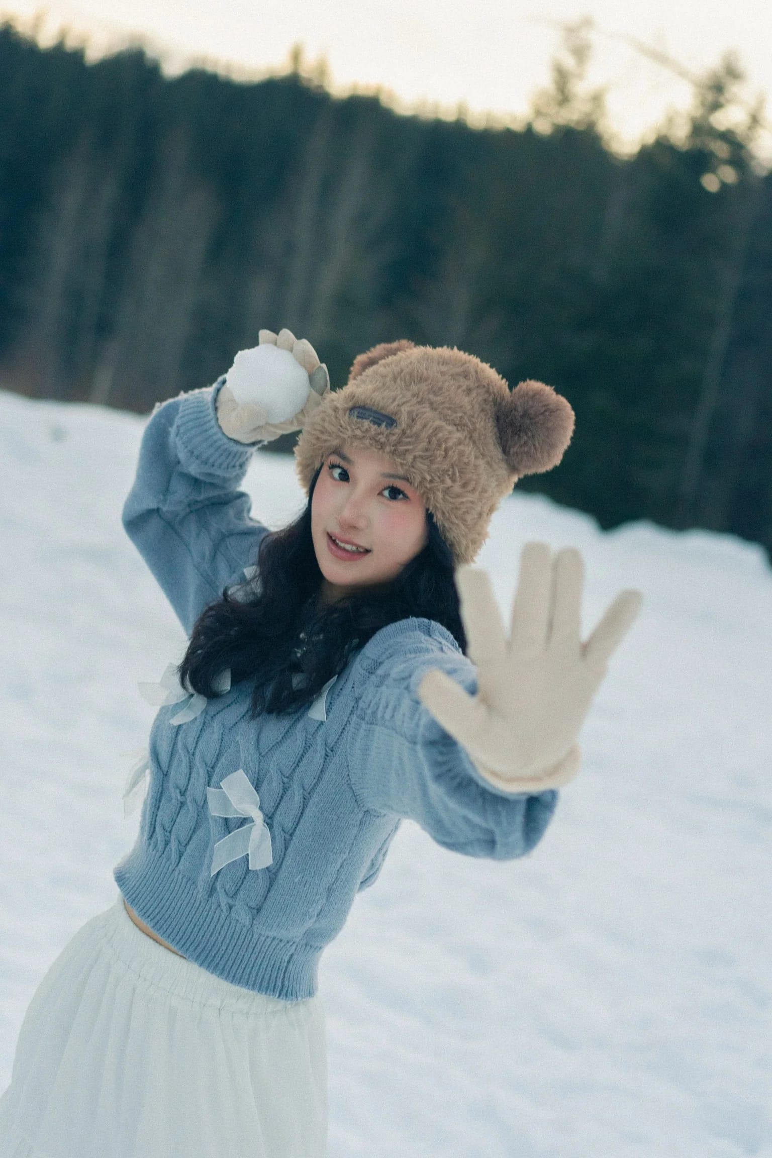 A woman reaching an open mitten toward the camera in the snow