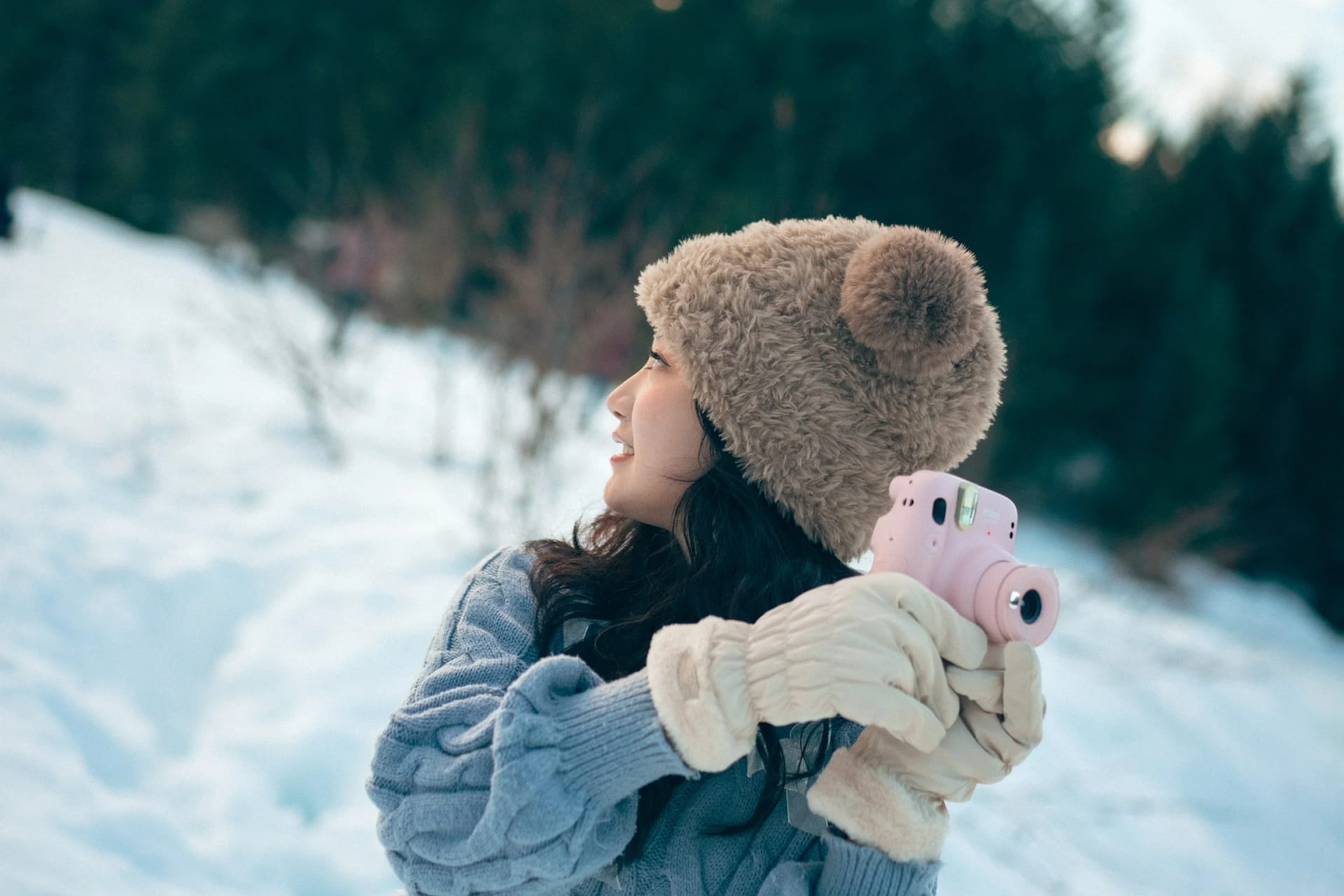 A woman holding a pink instant camera in a snowy clearing