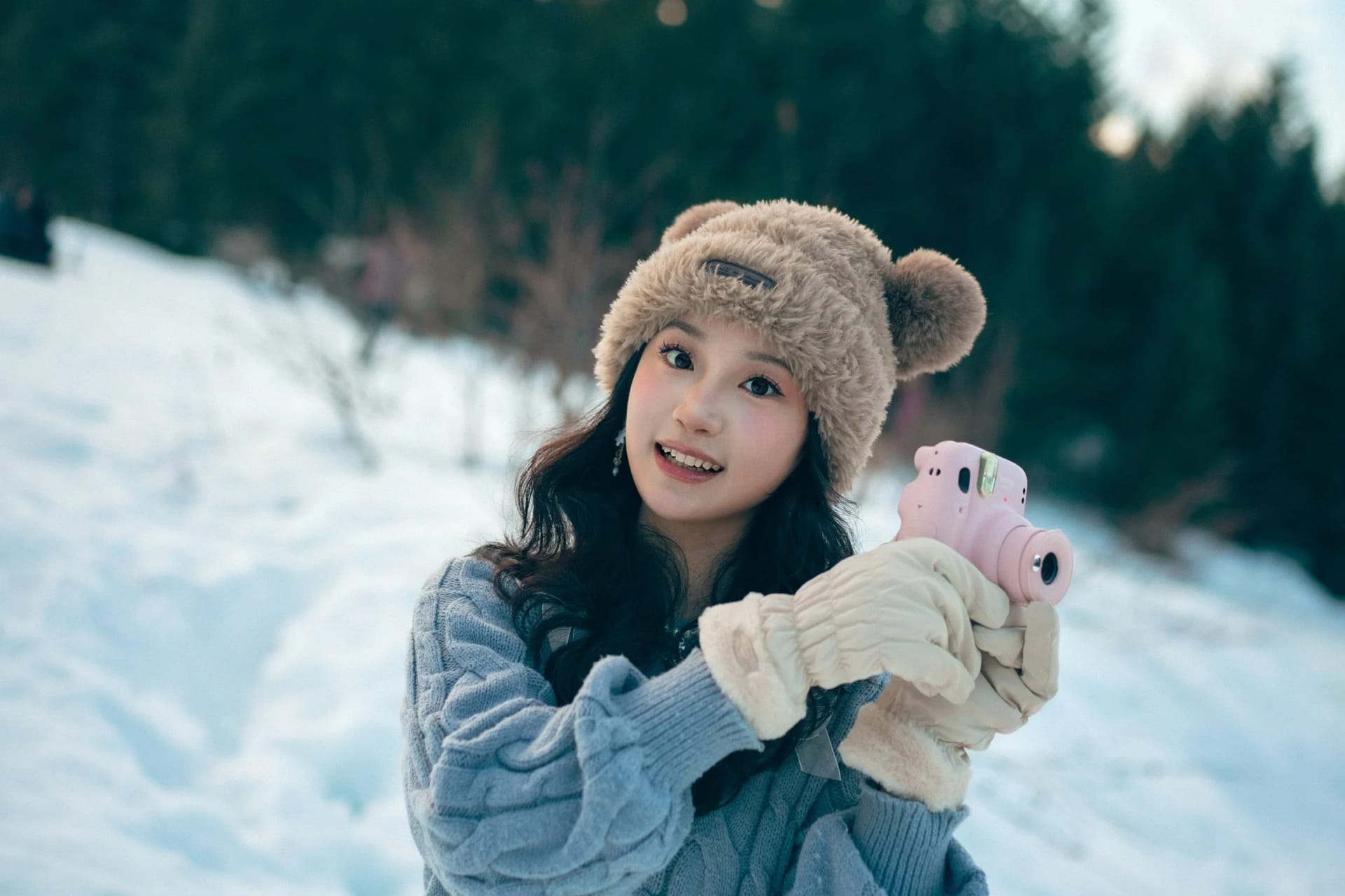 A woman wearing a bear-ear hat and holding a pink camera