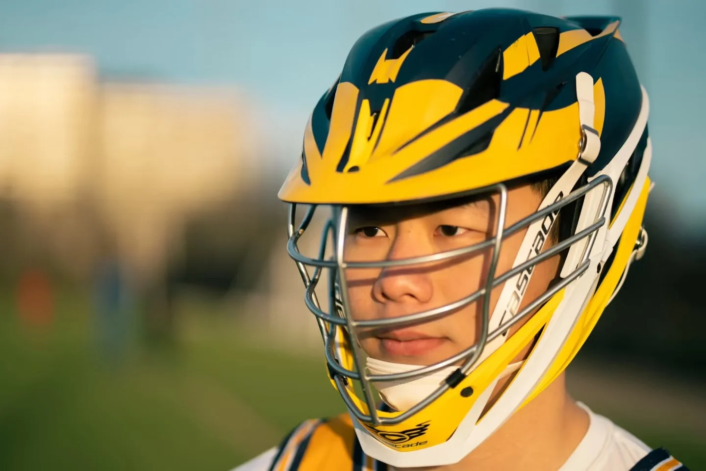 A close portrait of a lacrosse player through a yellow helmet guard