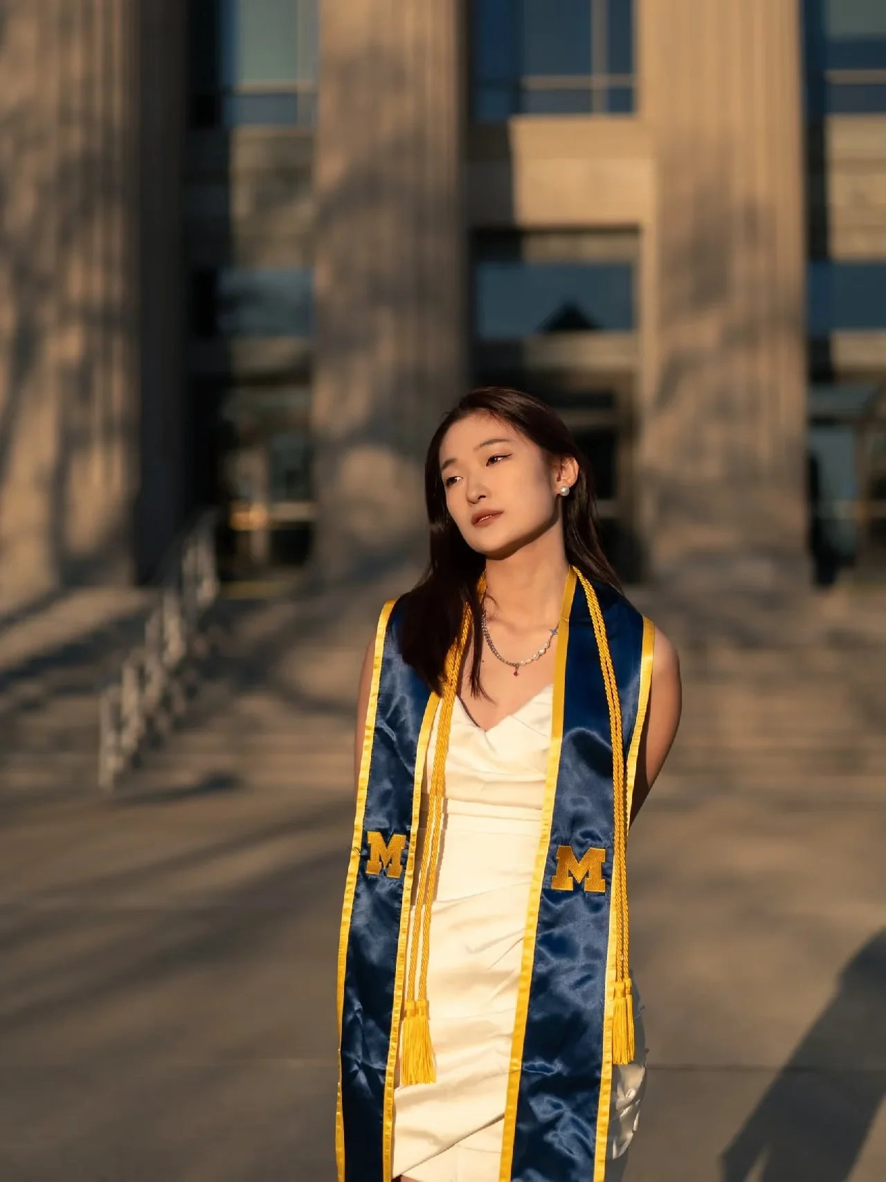 A graduate in warm sunlight beside a row of stone columns