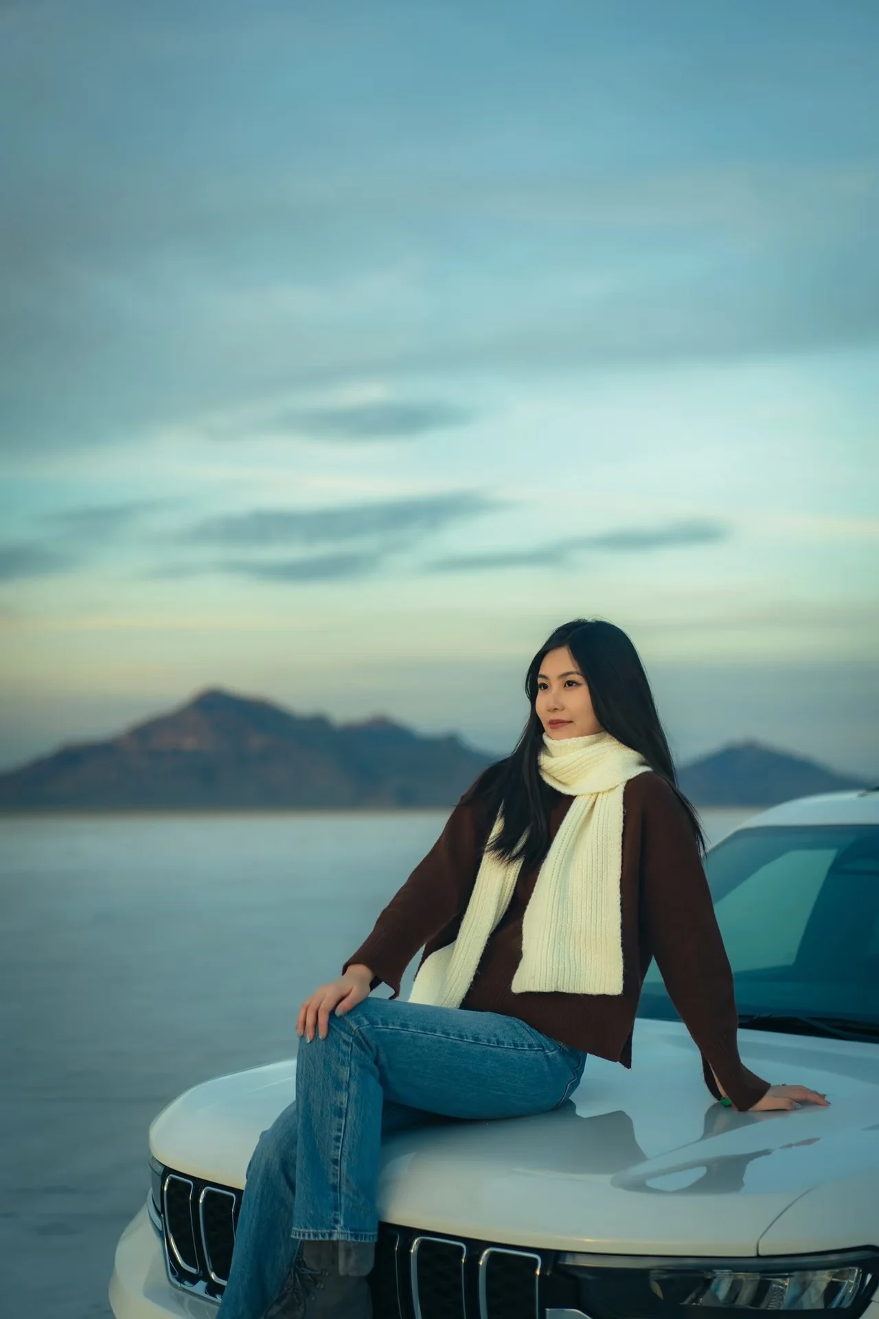 A woman seated on the hood of a car beneath a broad blue sky
