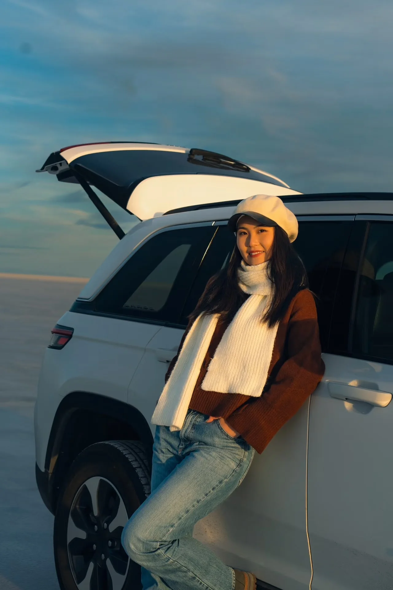 A woman leaning against a white car with its rear hatch open