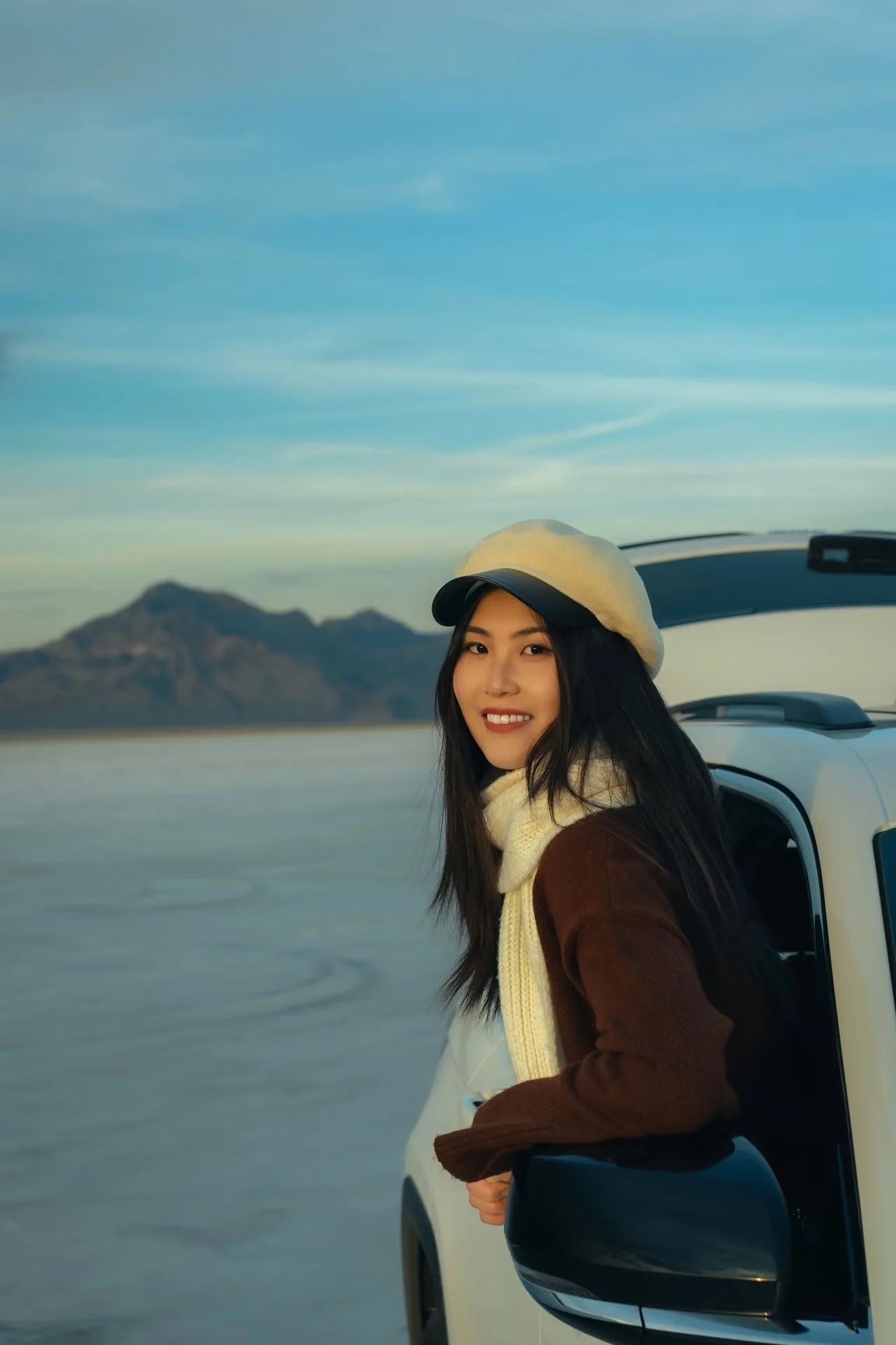 A woman in a cream cap sitting in an open car doorway