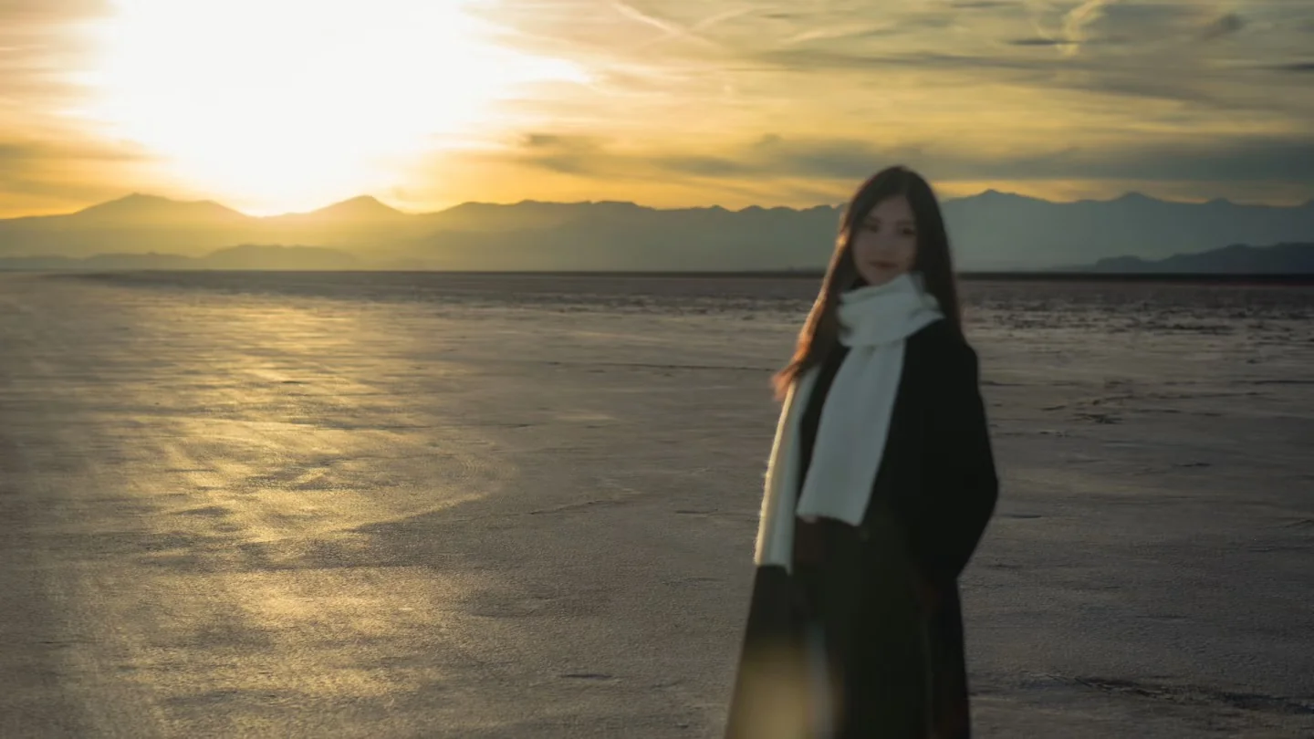 A woman standing on the salt flats as the sun sets behind the mountains