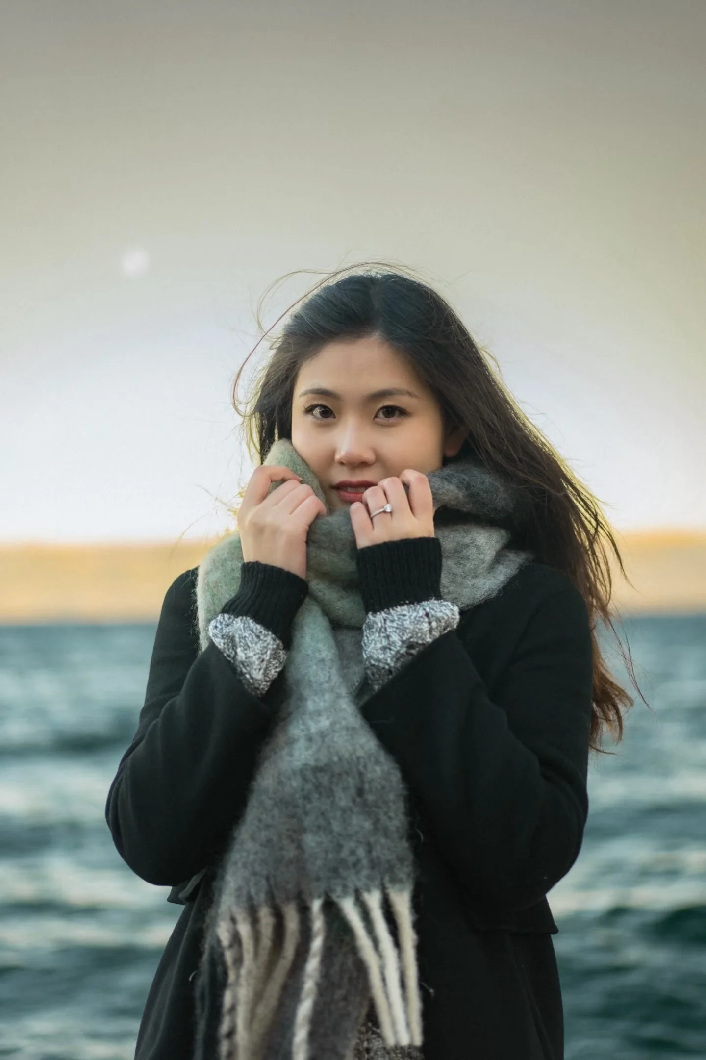 A woman holding her scarf with the lake behind her