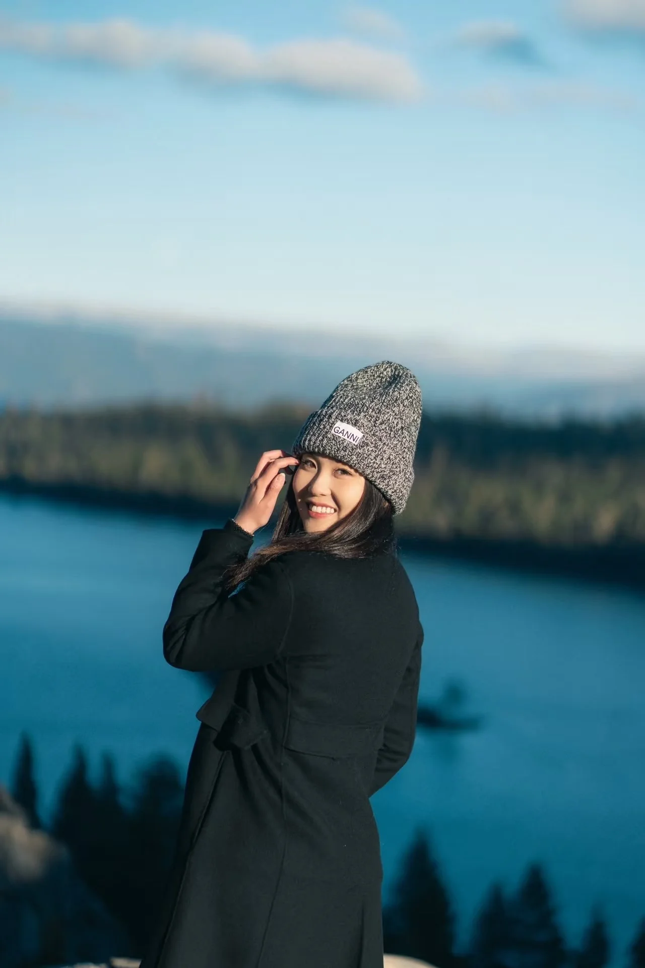 A smiling woman in a knit hat above the blue lake and forested shore