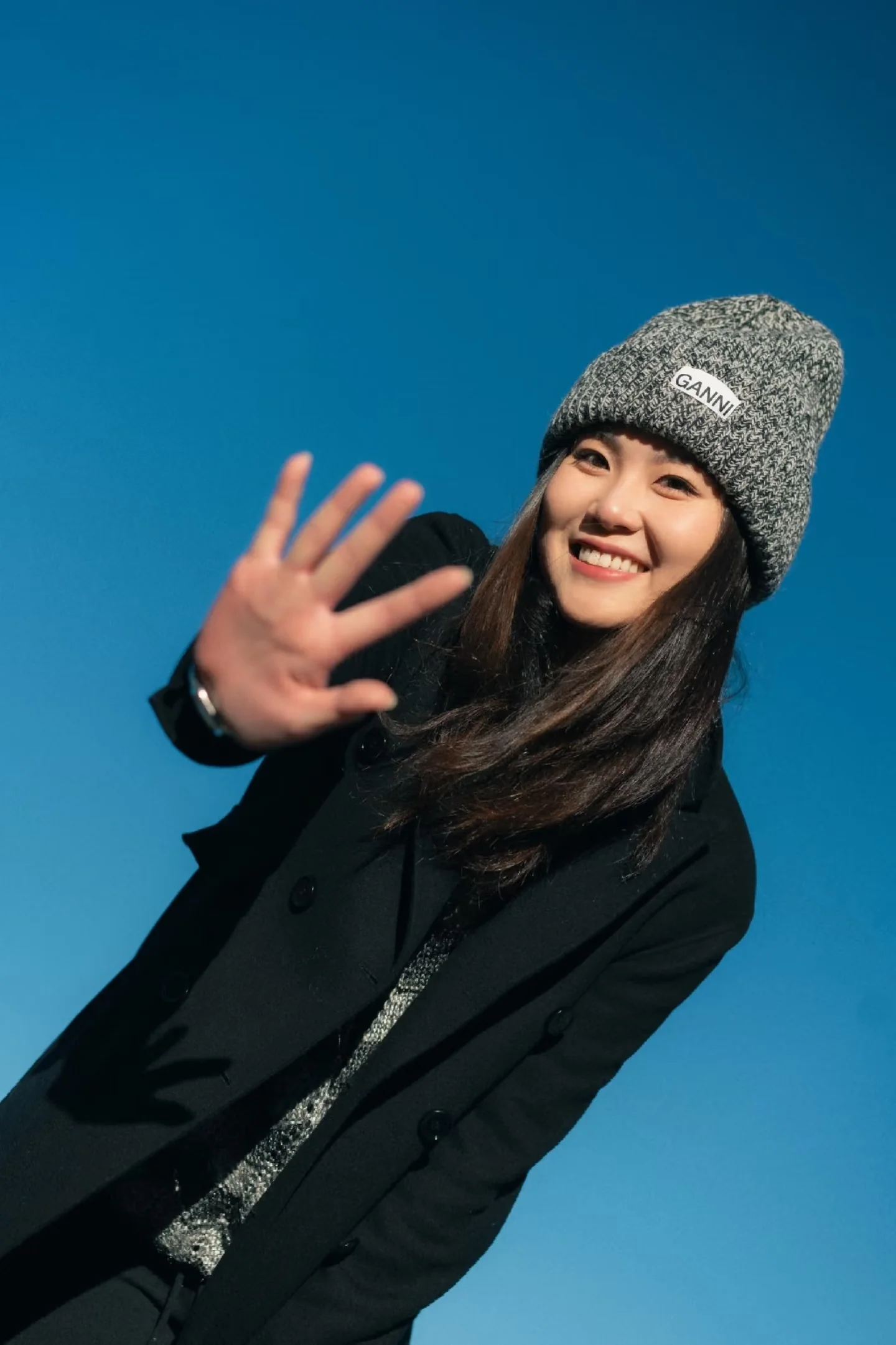 A smiling woman in a knit hat reaching toward the camera against a blue sky