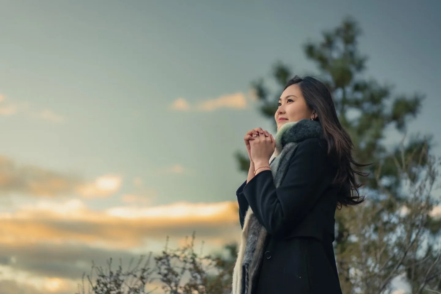 A woman in a dark coat beneath a softly lit evening sky