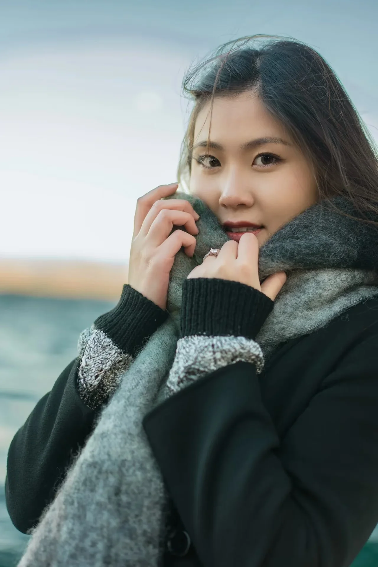A close portrait of a smiling woman wrapped in a gray scarf